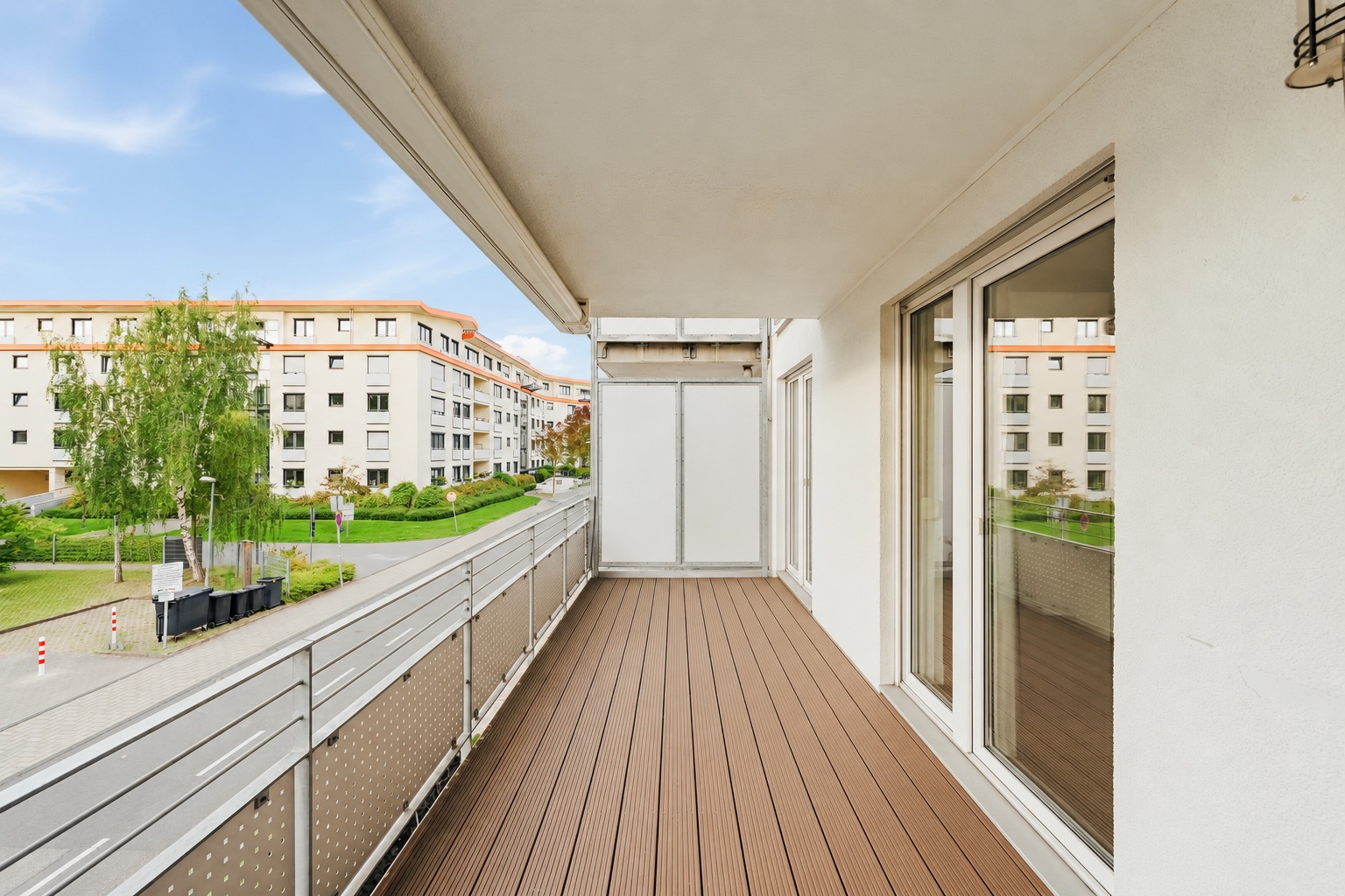 Moderner Balkon mit Holzfußboden und Glasgeländer, Blick auf Wohnhäuser und Straße.