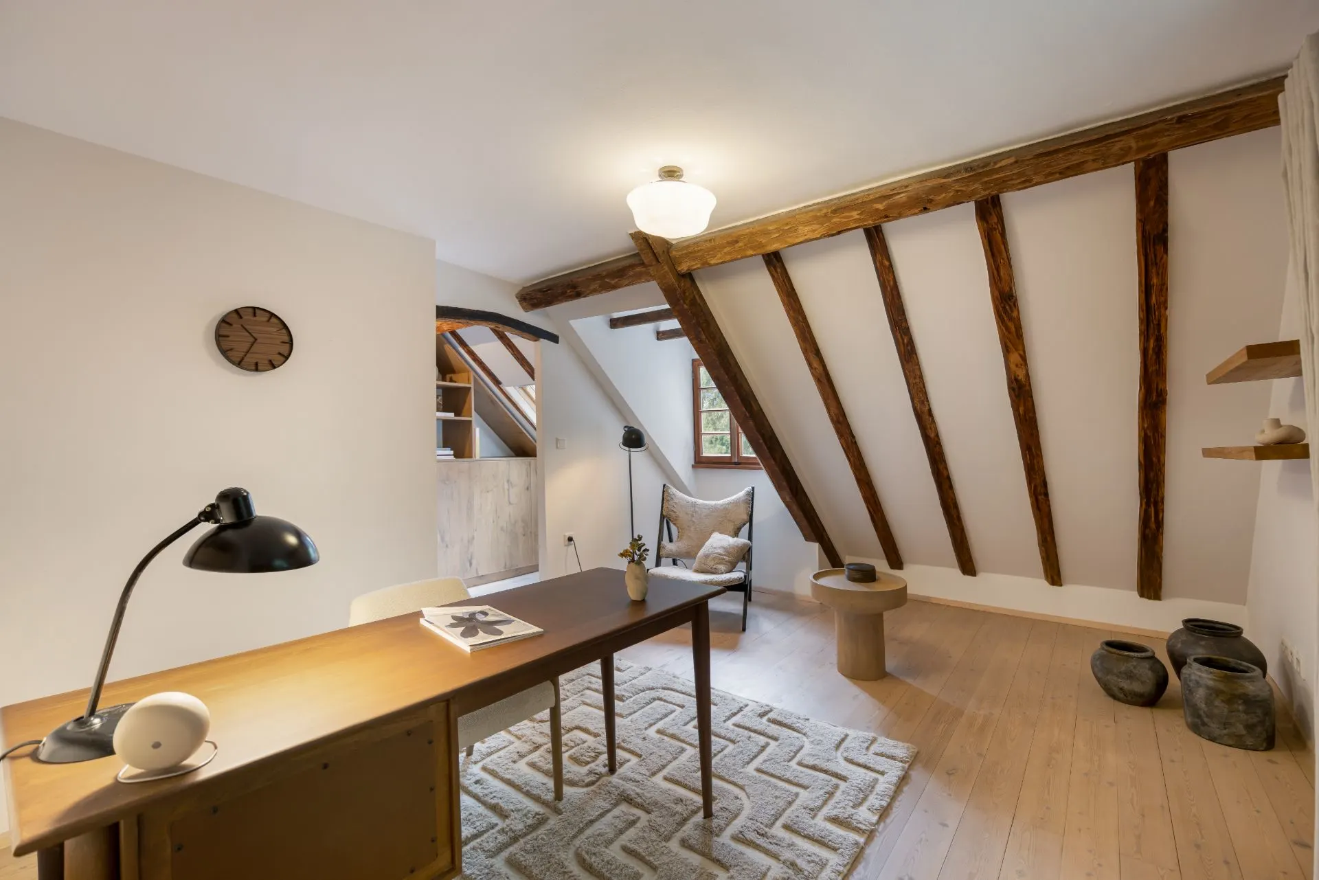 Helles Arbeitszimmer mit Schreibtisch, Sessel, Holzbalken und schräger Decke.