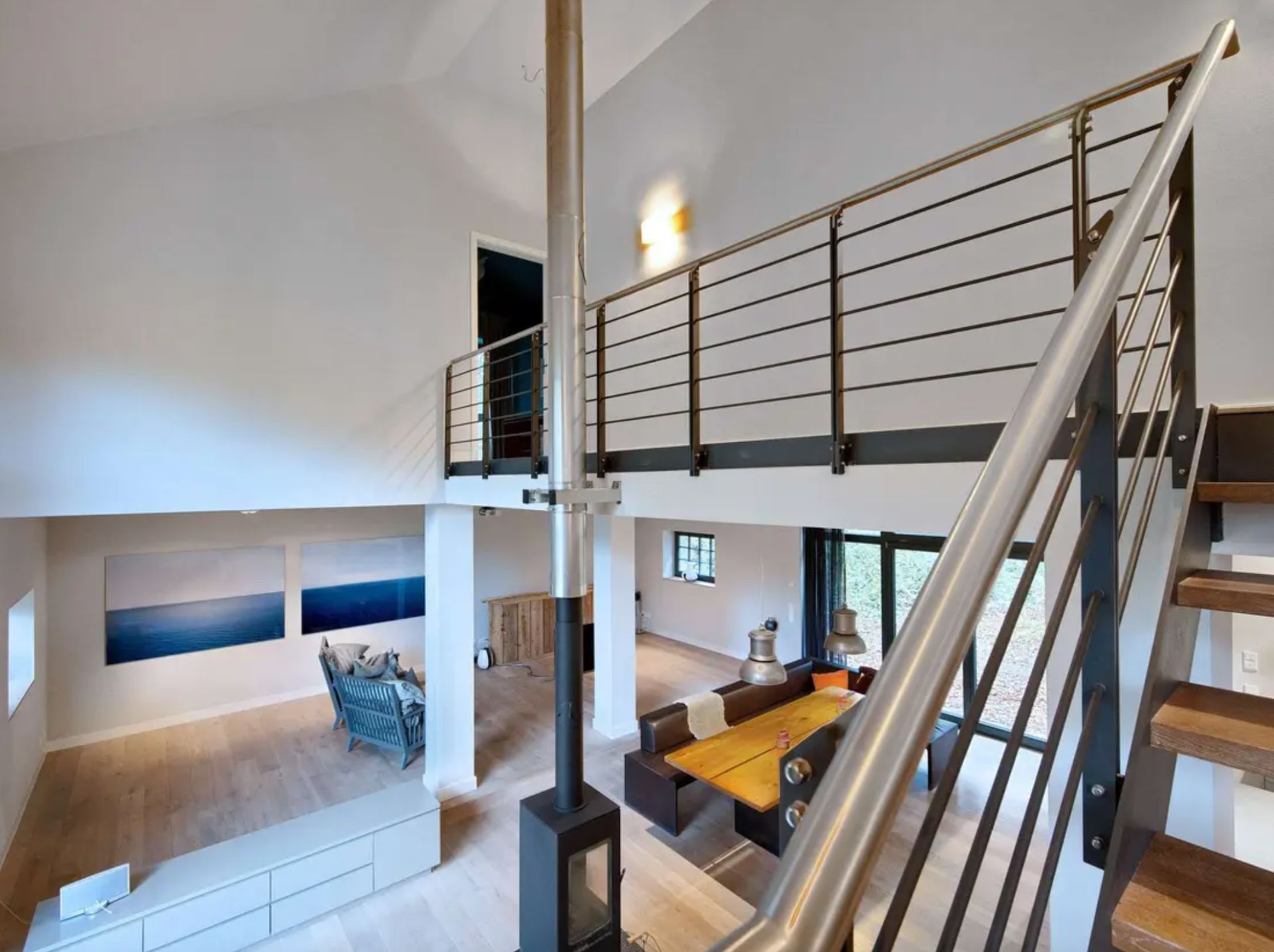 Modernes Wohnzimmer mit offener Galerie, Holzboden, Couch, Esstisch und Kaminofen.