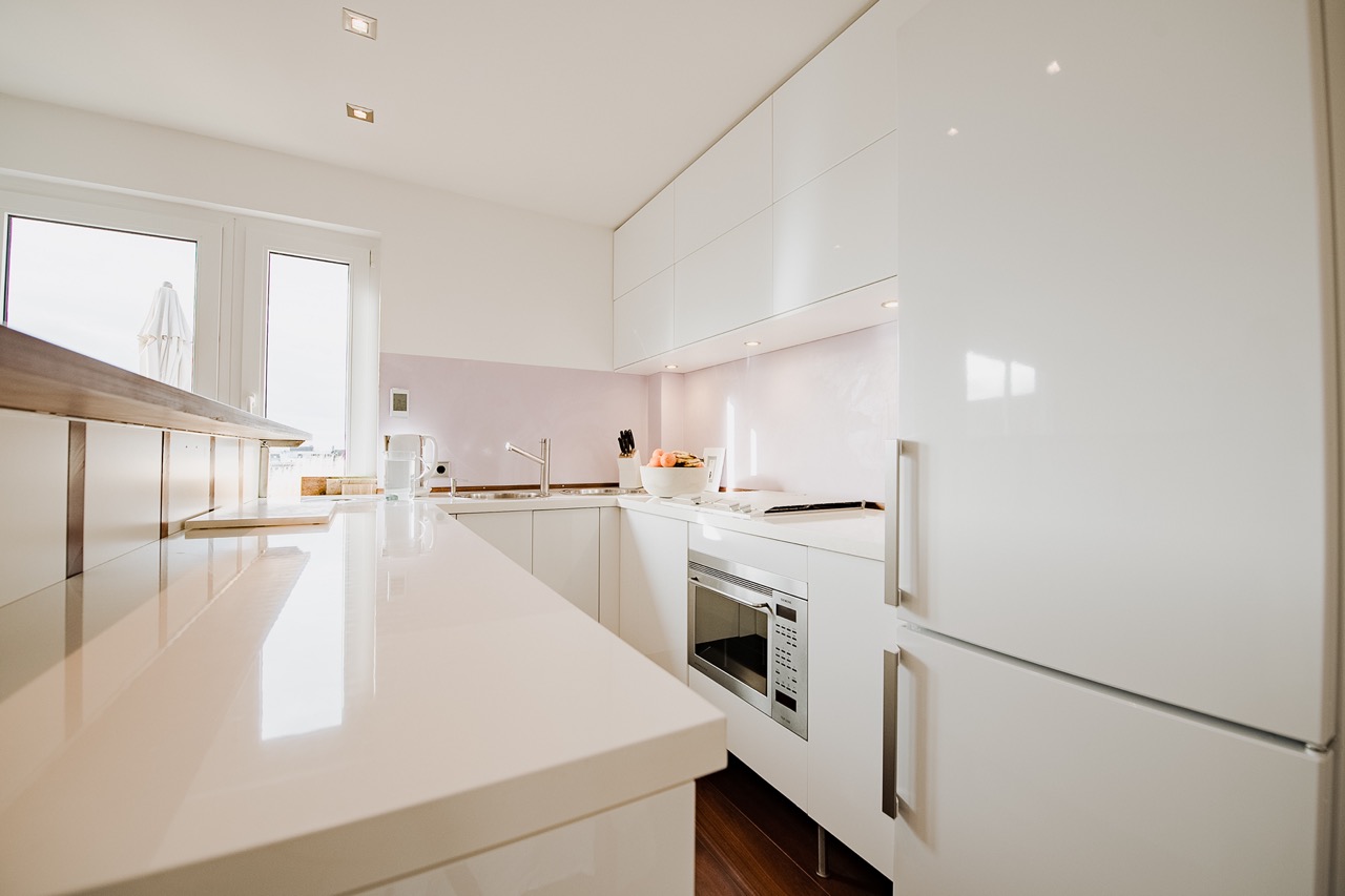 Moderne, helle Einbauküche mit weißen Schränken, Kühlschrank, Herd und Spüle.
