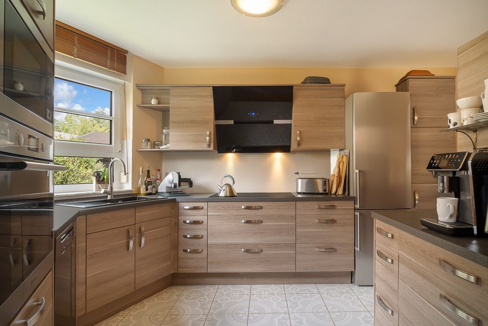 Moderne Küche mit Holzfronten, großem Fenster, Edelstahlgeräten und Kaffeemaschine.