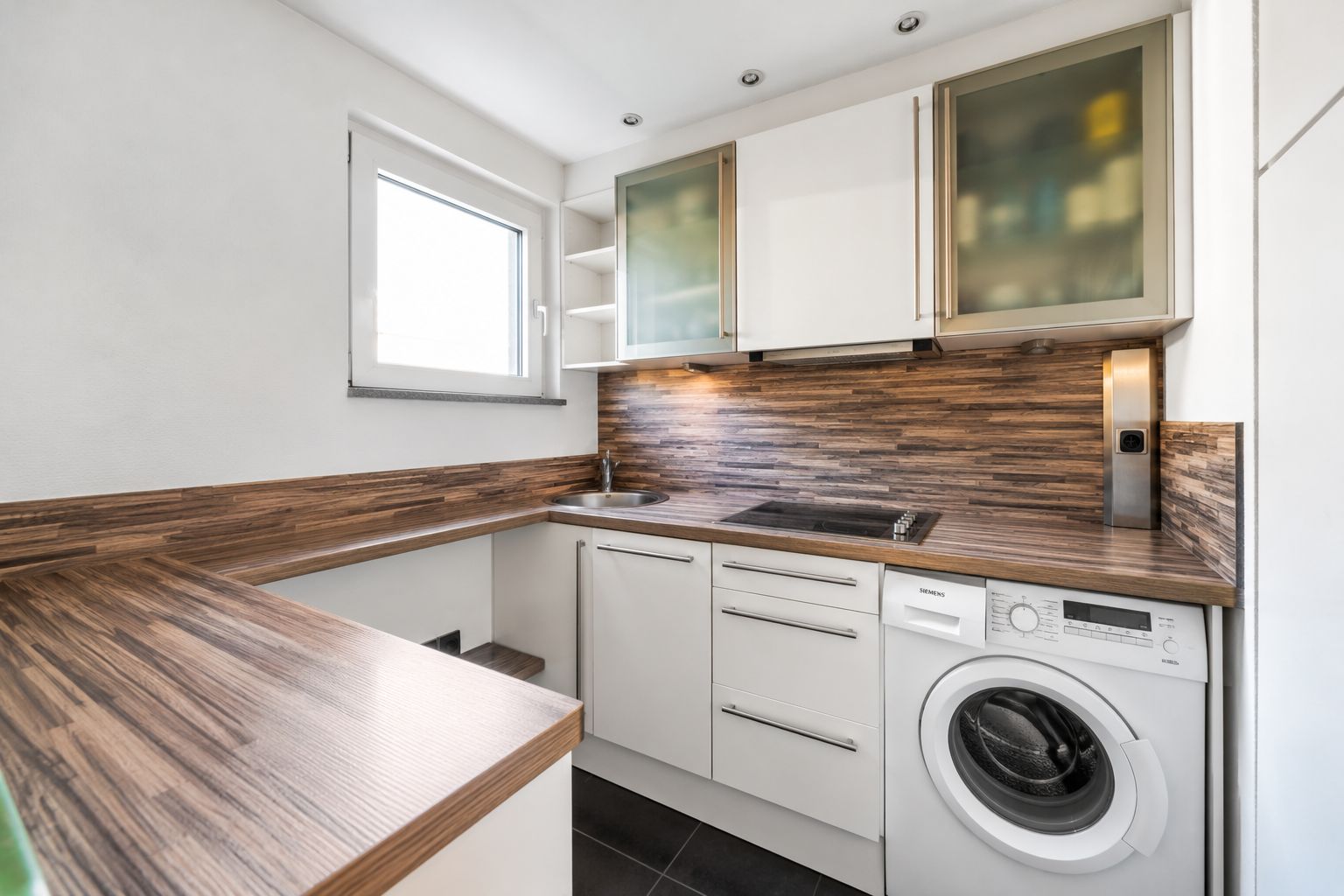 Moderne Einbauküche mit Holzarbeitsplatte, Herd, Spüle und Waschmaschine unter dem Fenster.