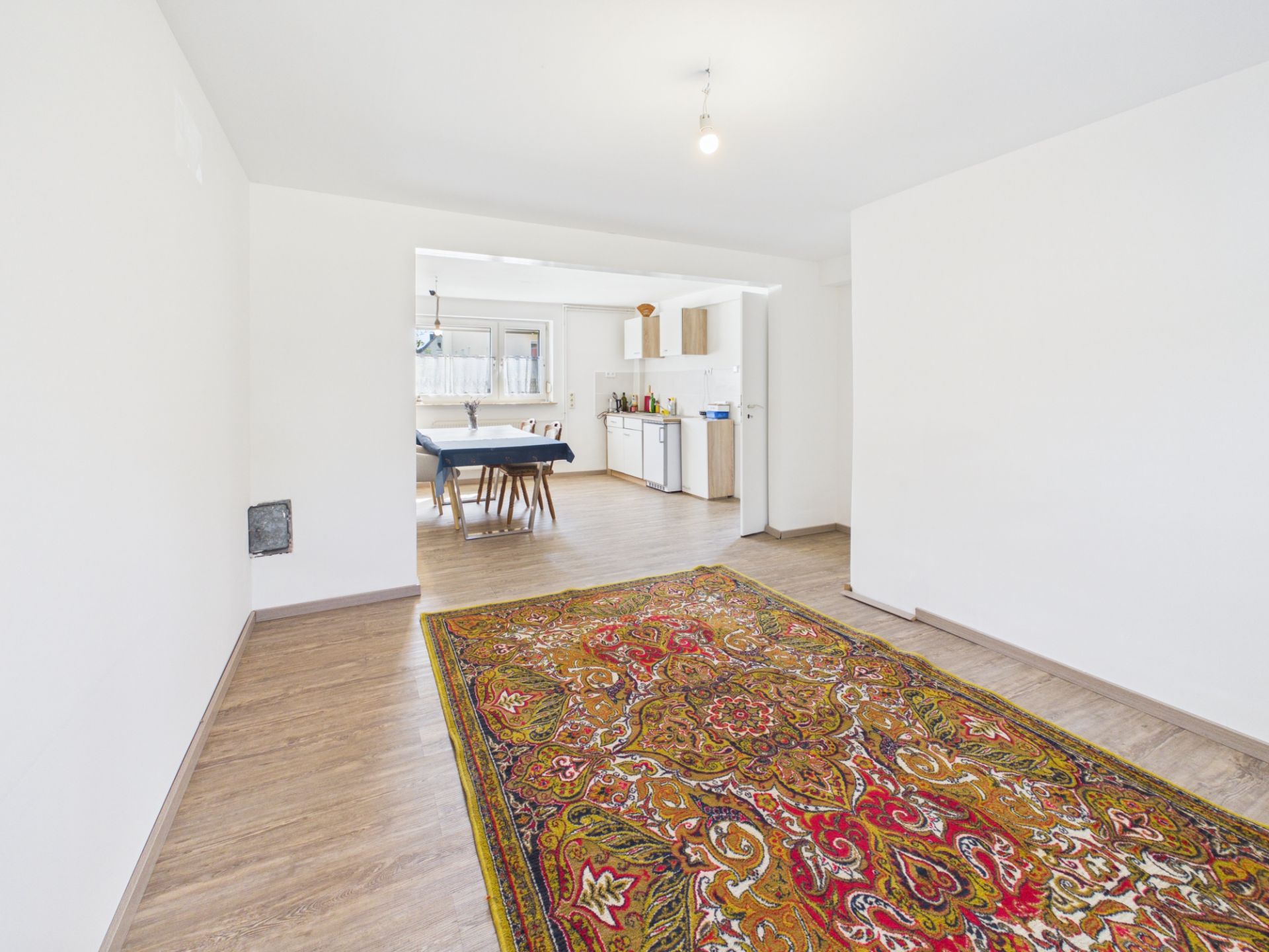 Helles Wohnzimmer mit Teppich, Blick auf Essbereich und offene Küche im Hintergrund.