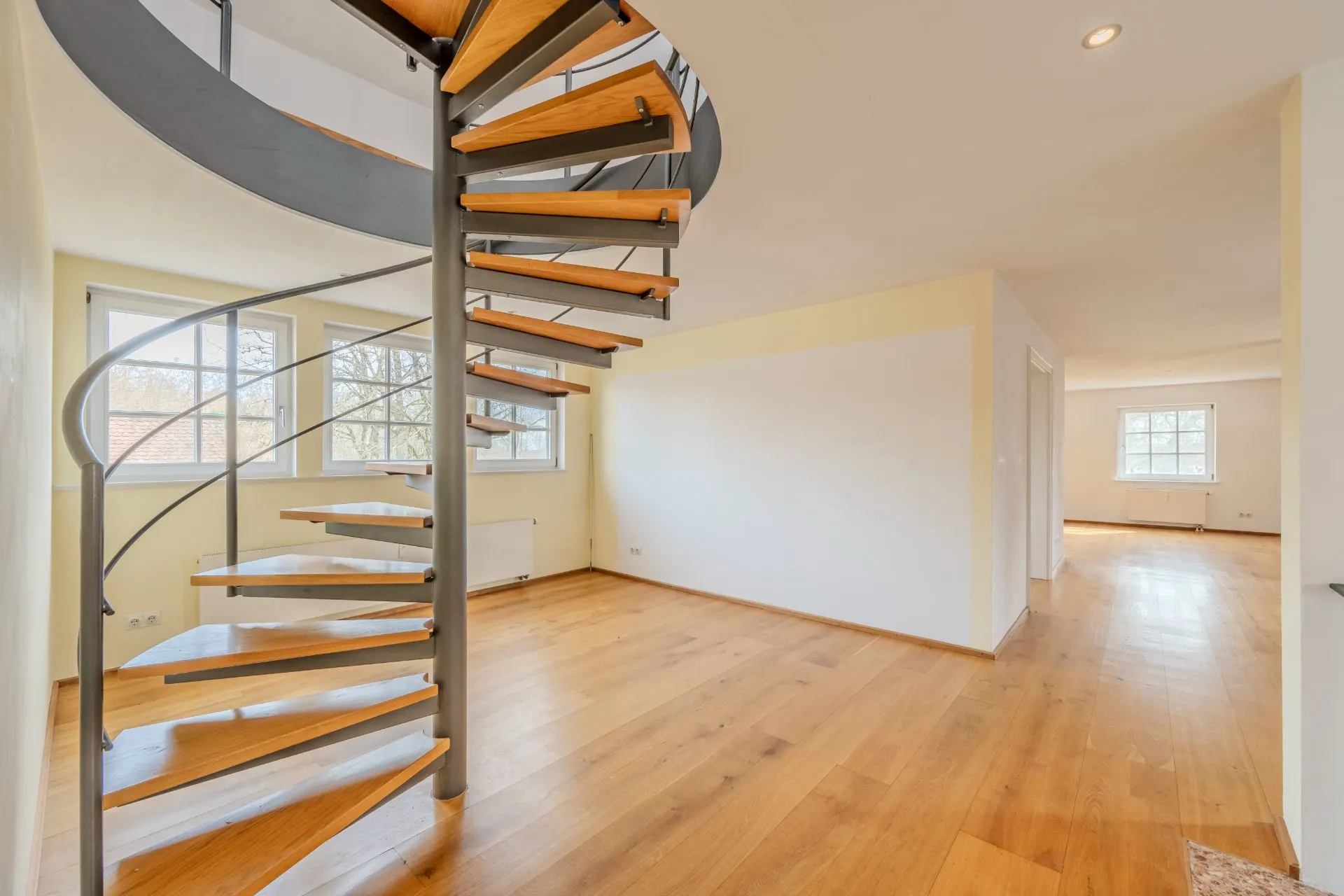 Helles Wohnzimmer mit Holzfußboden und moderner Wendeltreppe.