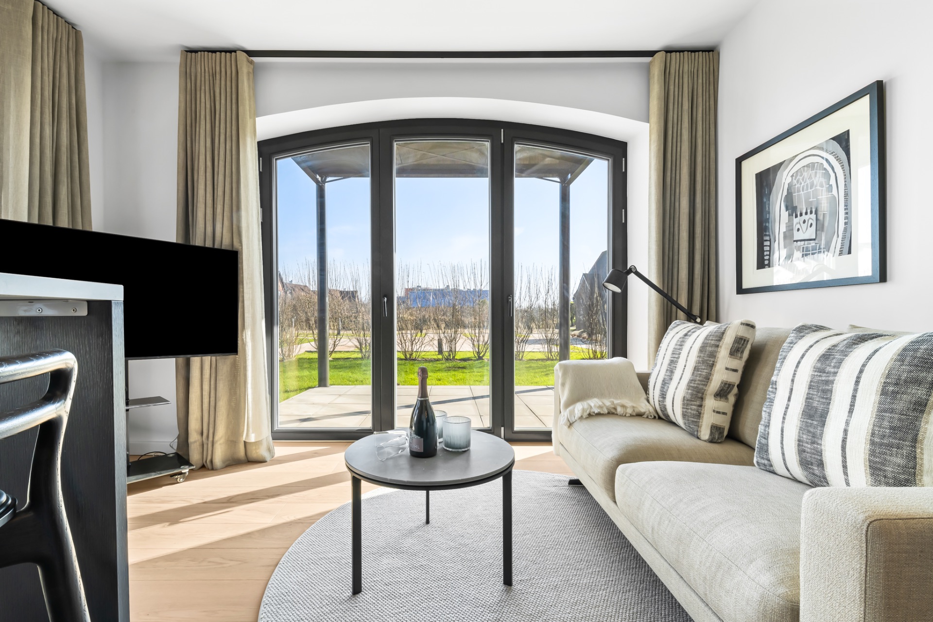 Helles Wohnzimmer mit großer Glasfront, Sofa, Couchtisch und Blick auf Garten.