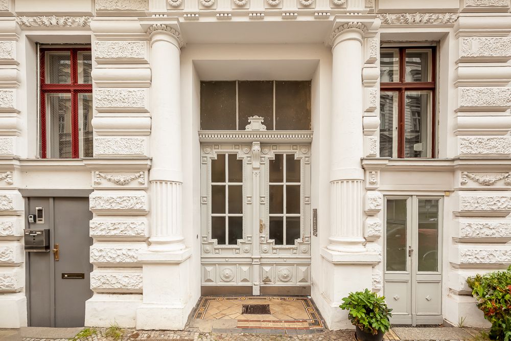 Eingangstür eines Altbau-Mehrfamilienhauses mit Säulen und Verzierungen.