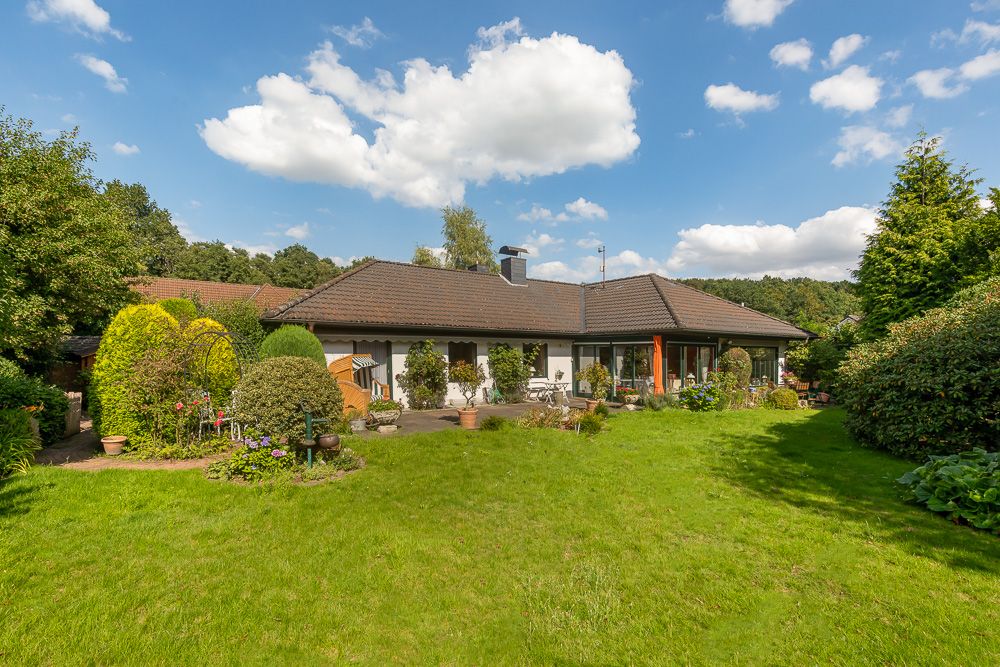 Einfamilienhaus mit großem Garten, Rasenfläche und vielen Pflanzen bei sonnigem Wetter.