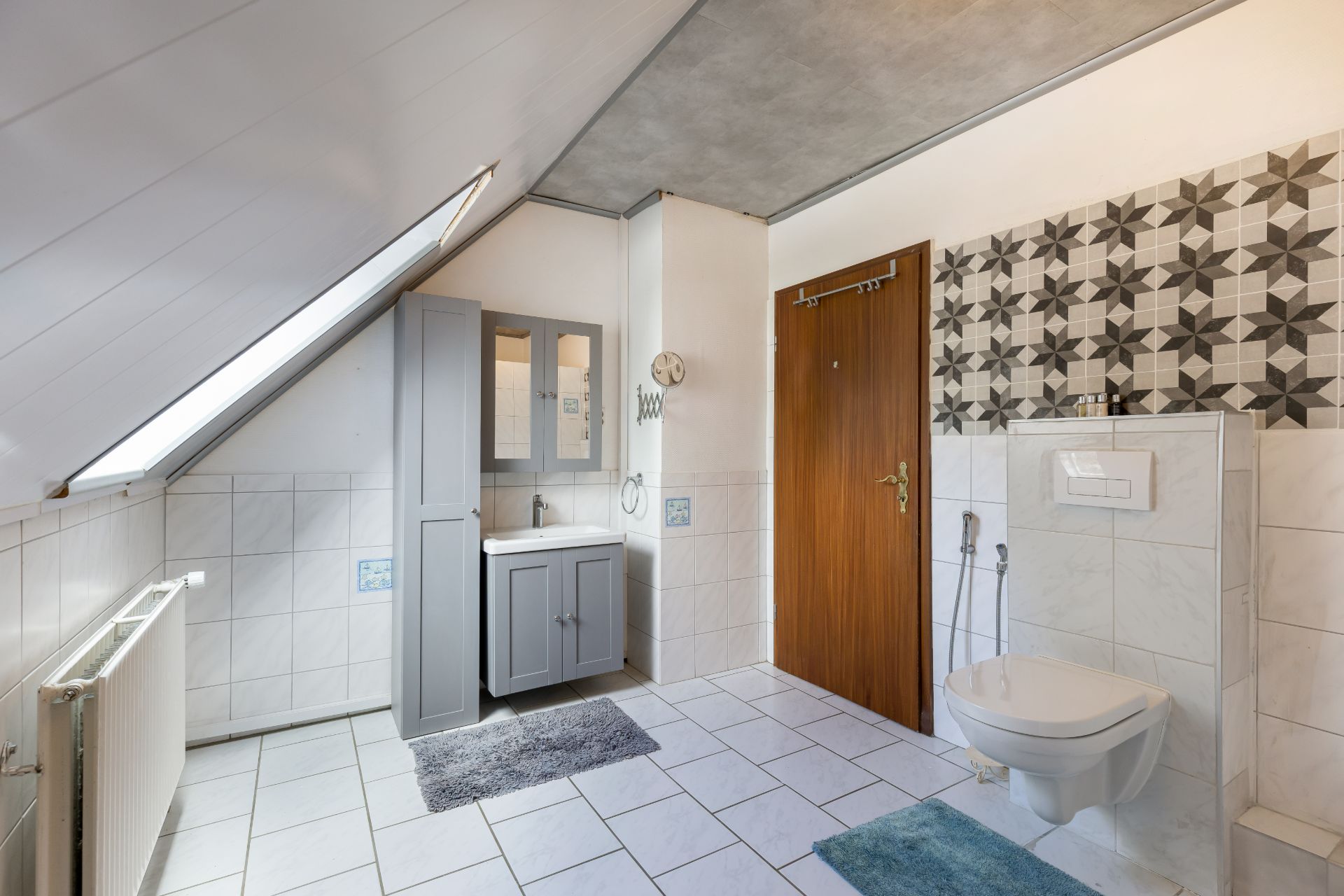 Modernes Badezimmer mit Dachfenster, grauem Waschtisch, Hängeschrank und WC an gefliester Wand.