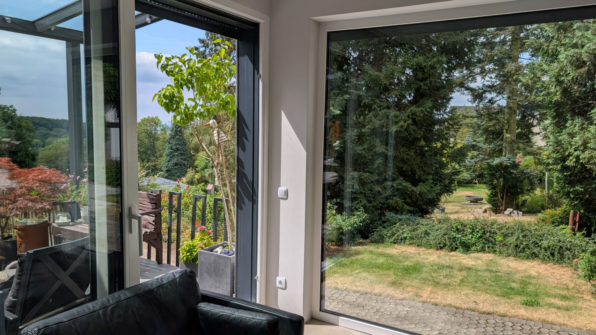 Wohnzimmer mit großen Fenstern und Blick auf einen grünen Garten mit Bäumen.