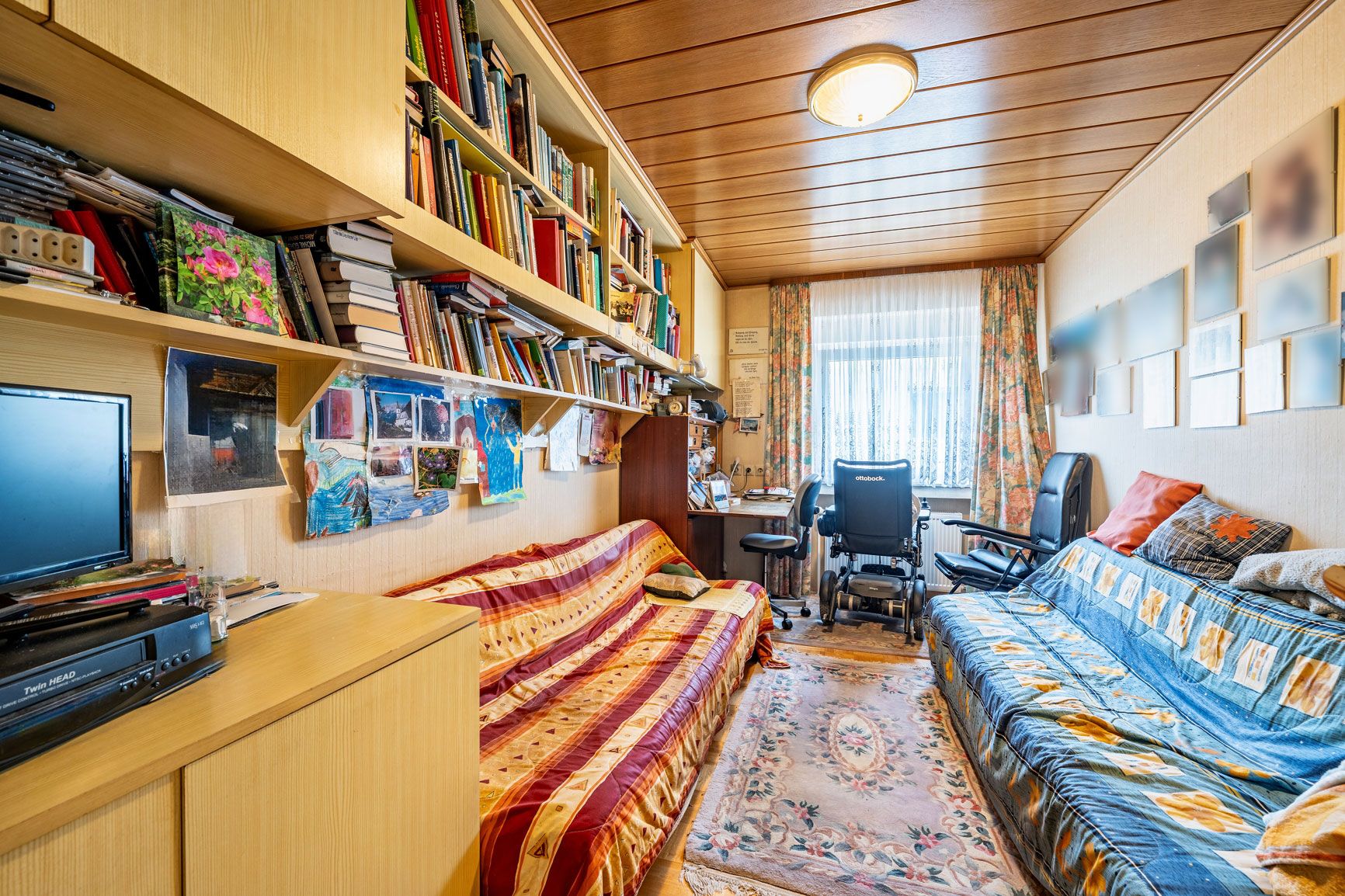 Wohnzimmer mit zwei Sofas, Bücherregalen, Teppich und Schreibtisch am Fenster.