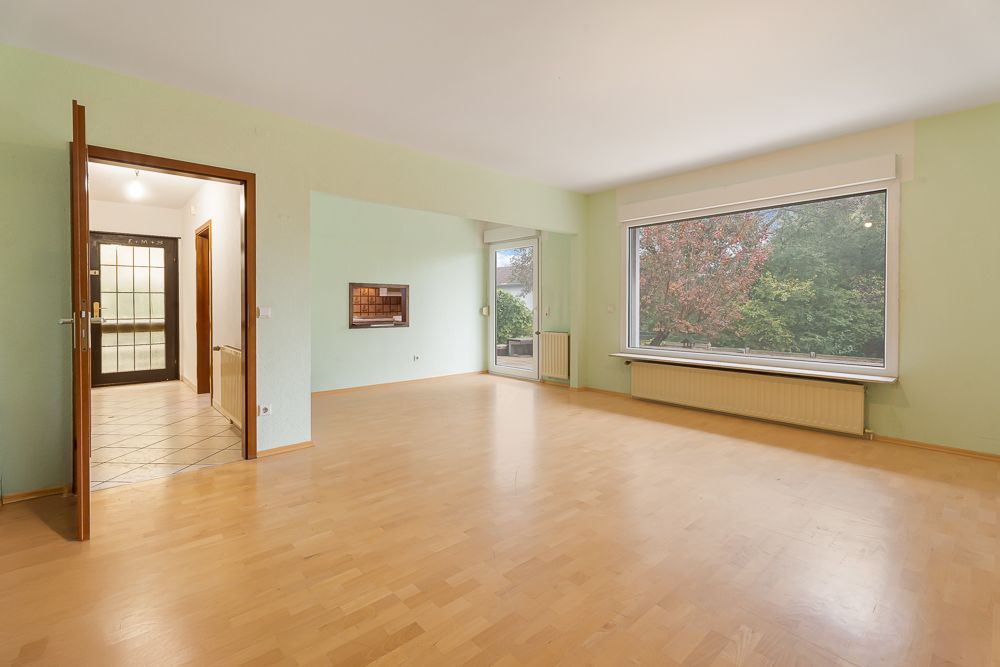 Helles Wohnzimmer mit Parkettboden, großem Fenster und Zugang zu Flur und Terrasse.