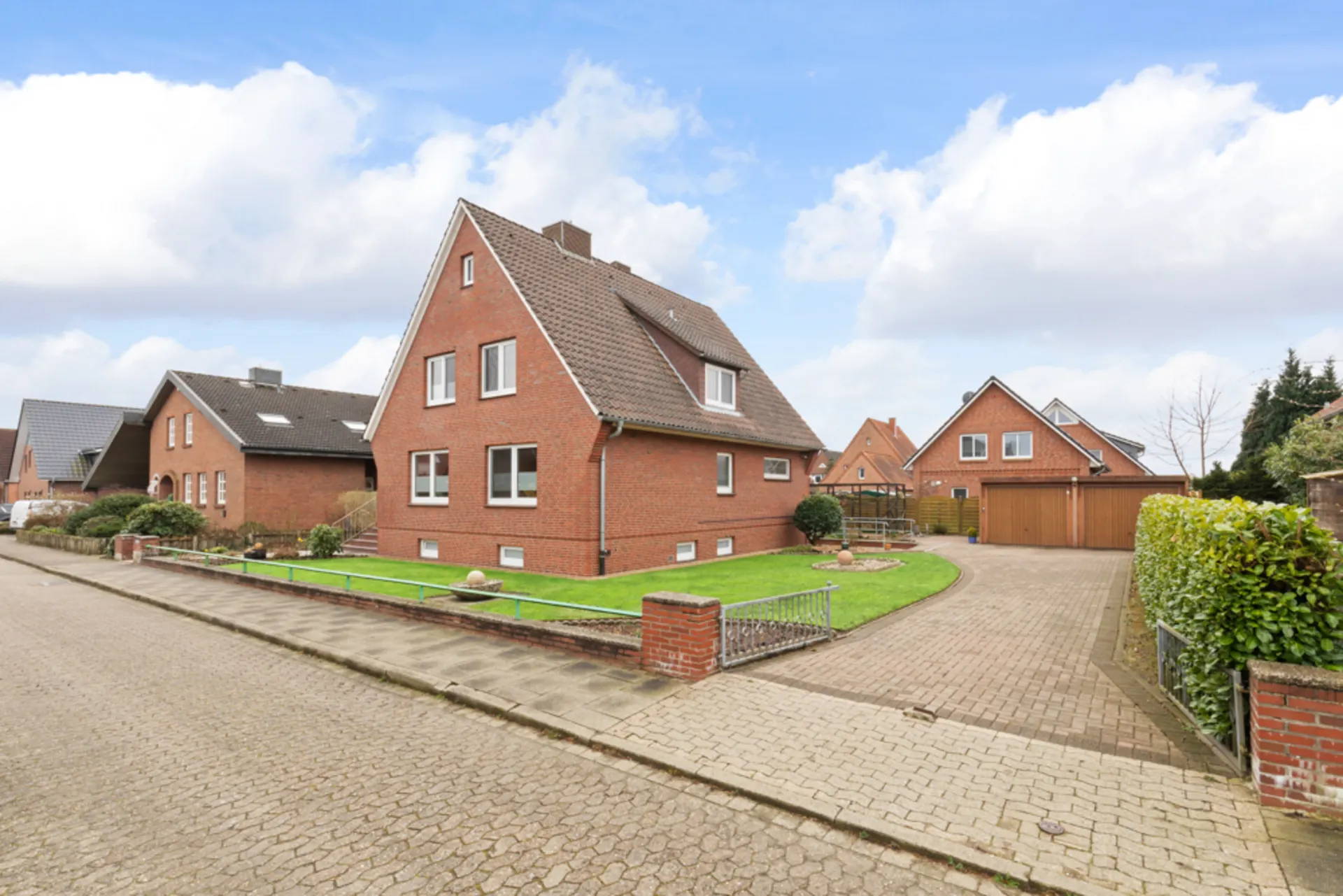 Backsteinwohnhaus mit Satteldach, Vorgarten und gepflasterter Einfahrt in ruhiger Wohnstraße.