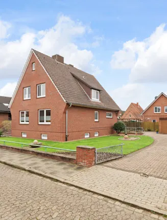 Backsteinwohnhaus mit Satteldach, Vorgarten und gepflasterter Einfahrt in ruhiger Wohnstraße.