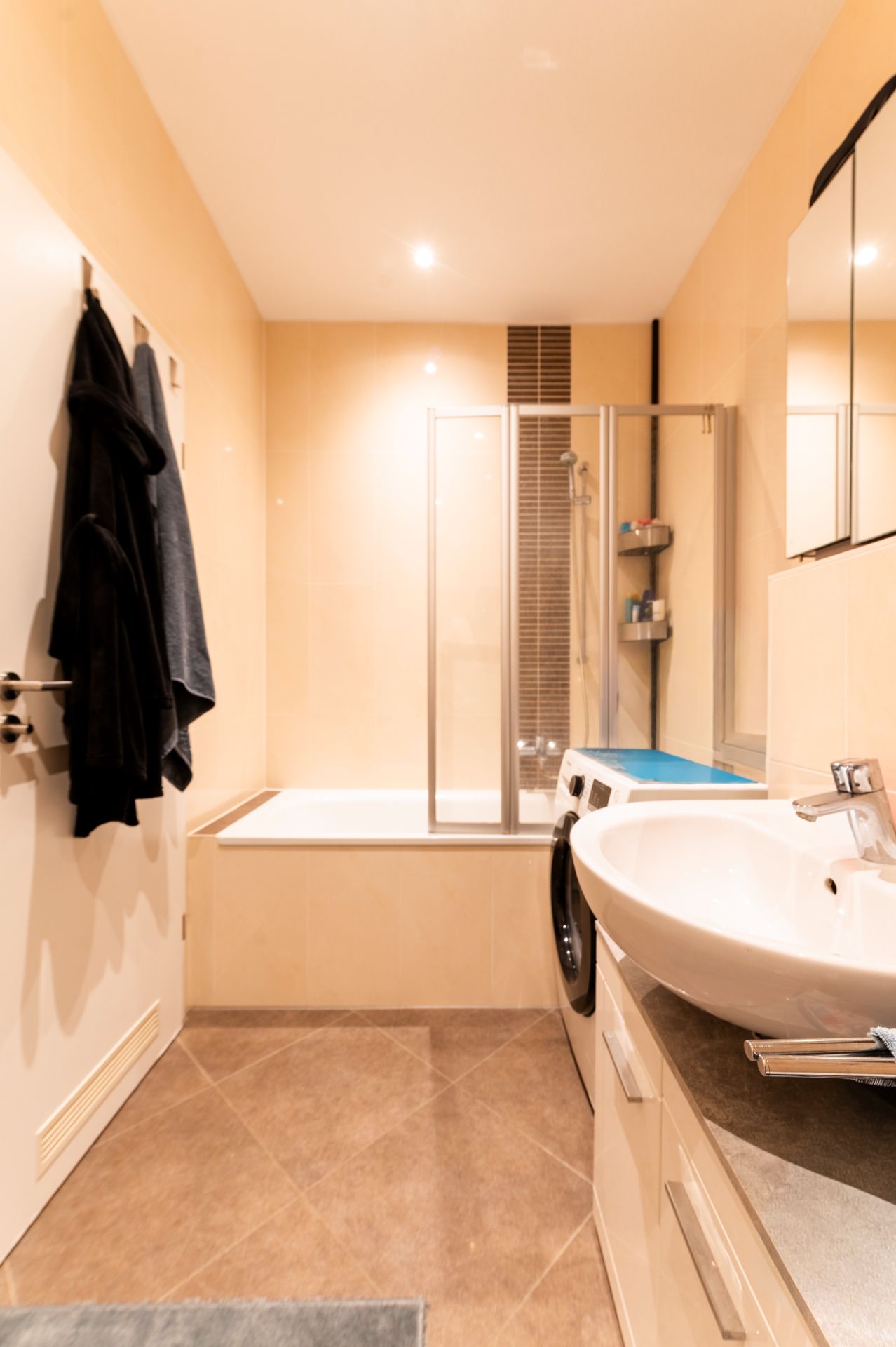 Modernes Badezimmer mit Badewanne, Waschmaschine, Waschbecken und Spiegel.