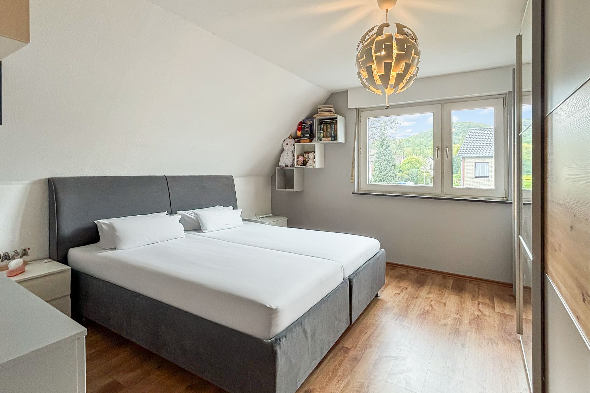 Helles Schlafzimmer mit Doppelbett, Holzfußboden und großem Fenster mit Blick nach draußen.