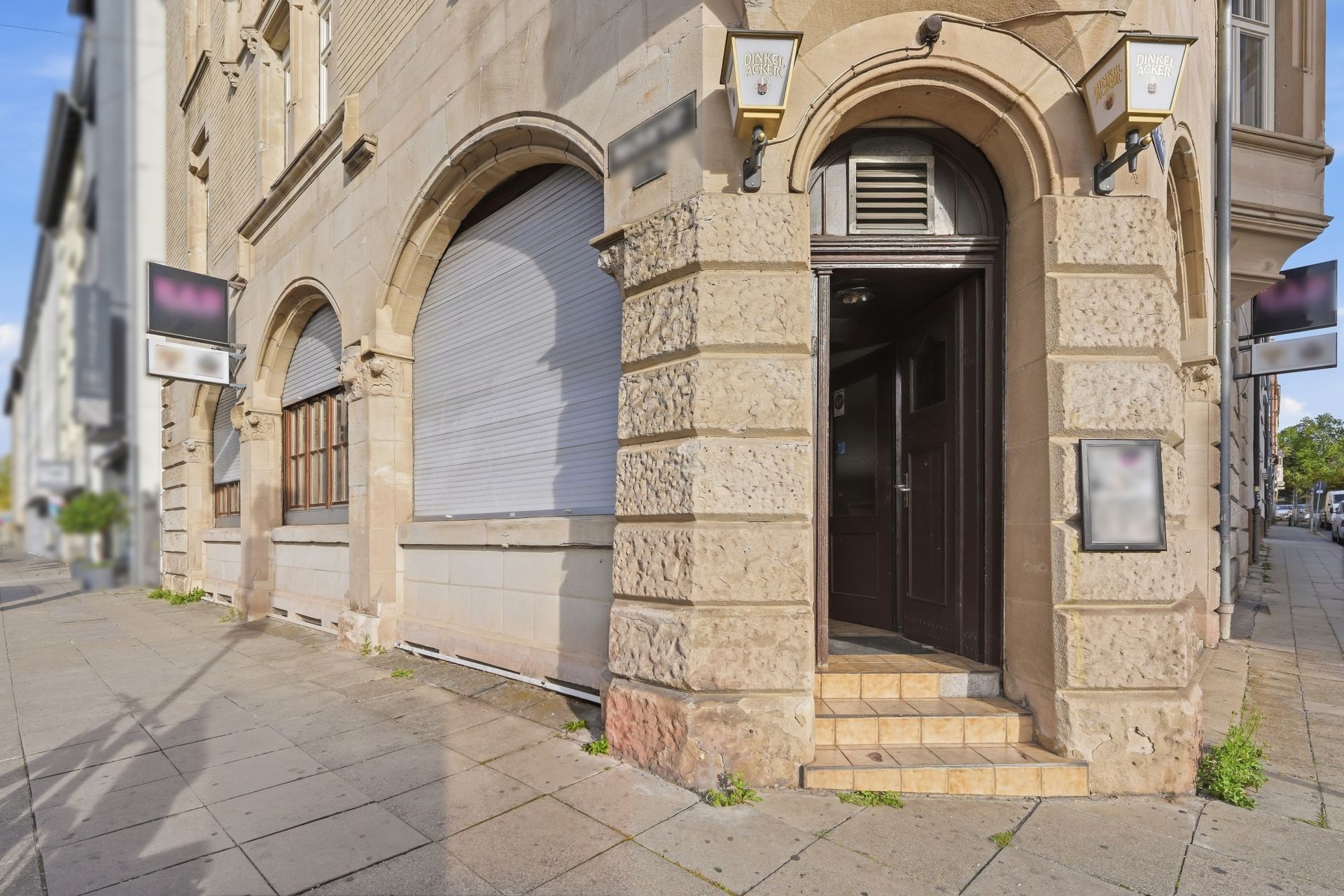 Eingang zu einem Altbau mit steinernen Bögen und geschlossenen Rollläden an der Straßenecke.