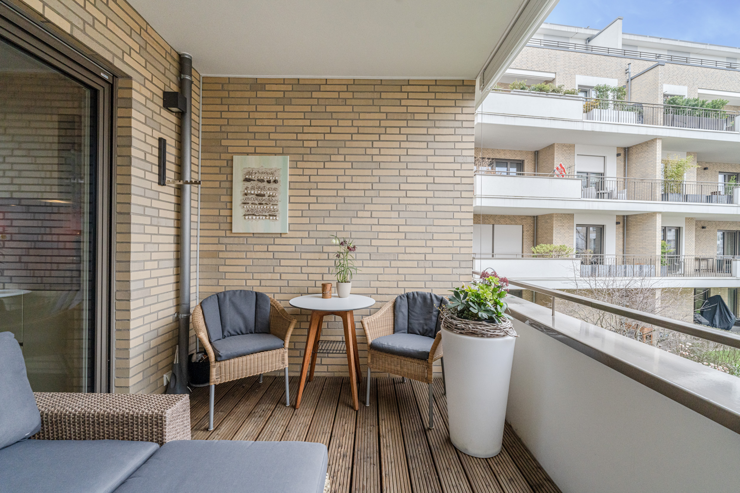 Überdachter Balkon mit Sitzgruppe, kleinem Tisch und Pflanztopf, Blick auf Nachbarbalkone.