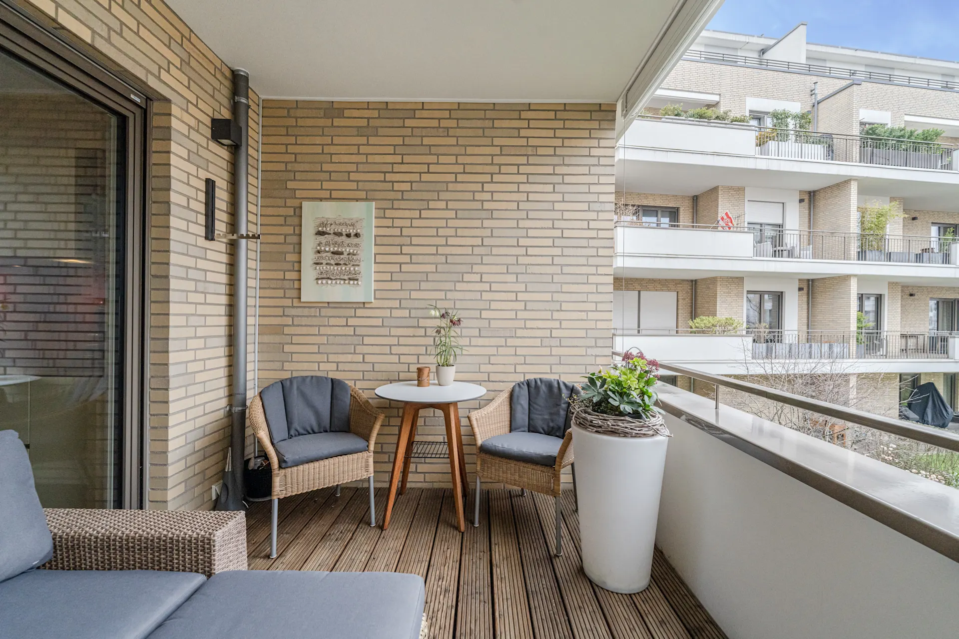 Überdachter Balkon mit Sitzgruppe, kleinem Tisch und Pflanztopf, Blick auf Nachbarbalkone.