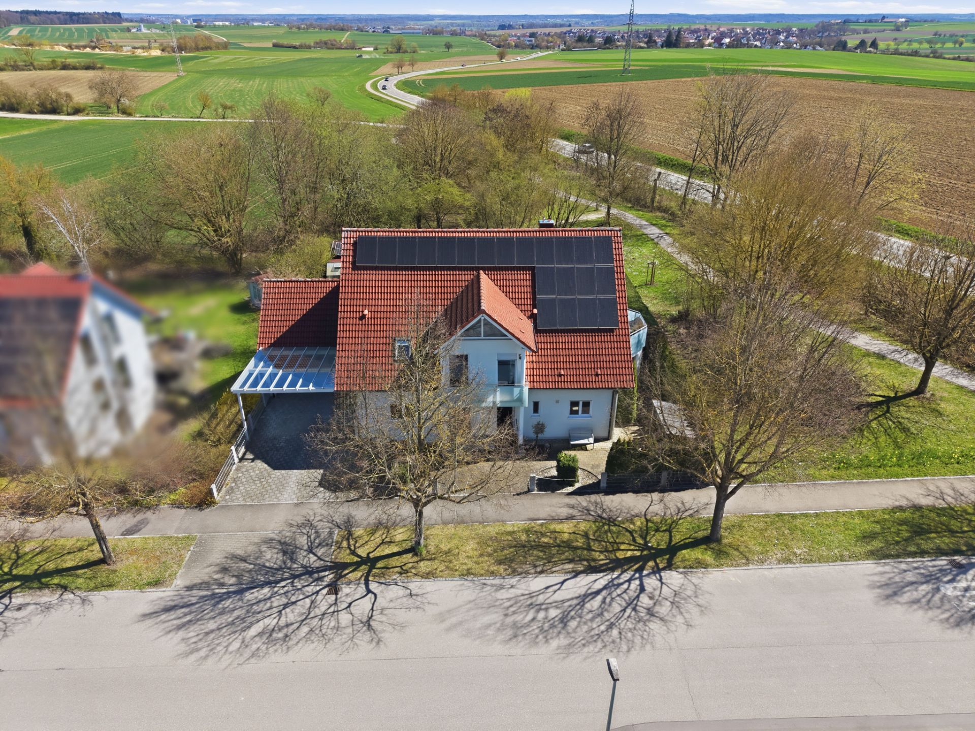 Einfamilienhaus mit rotem Dach und Solarpanels, umgeben von Bäumen und Feldern.