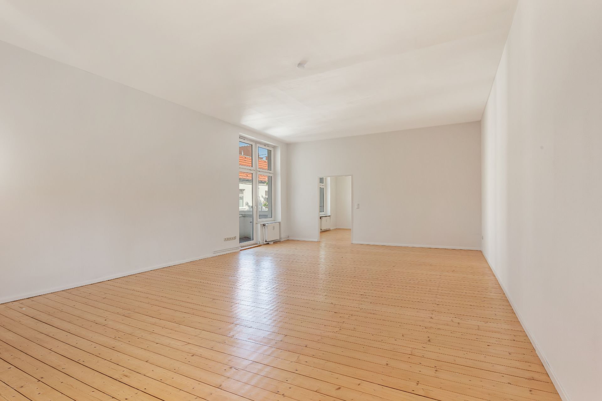 Helles, leeres Zimmer mit Holzboden und großen Fenstern.