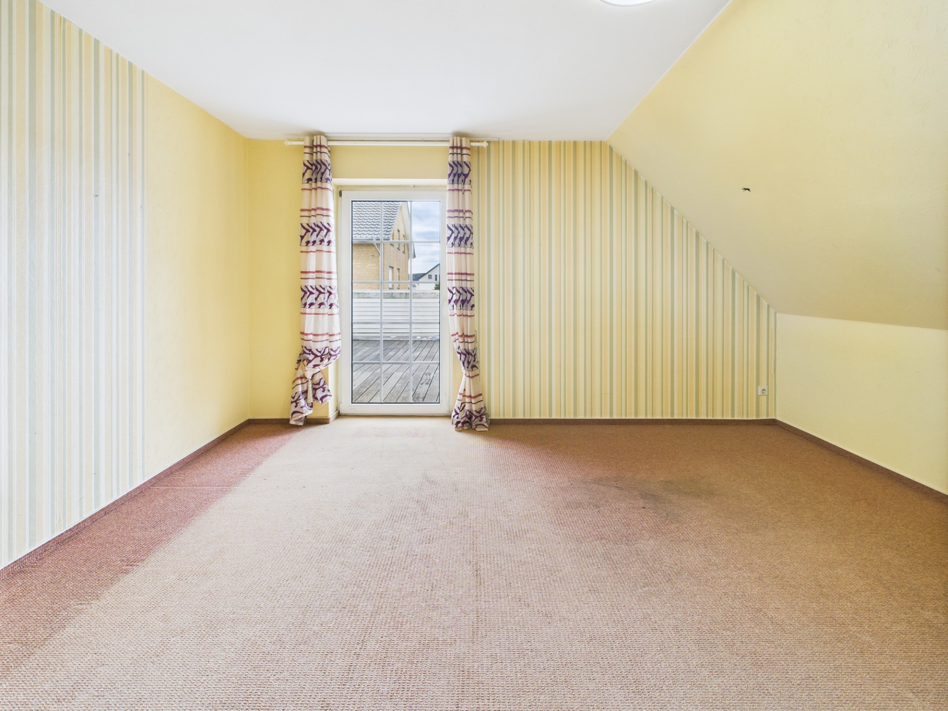Leeres Zimmer mit gelbem Teppich, gestreifter Tapete und Tür zu einem Balkon.