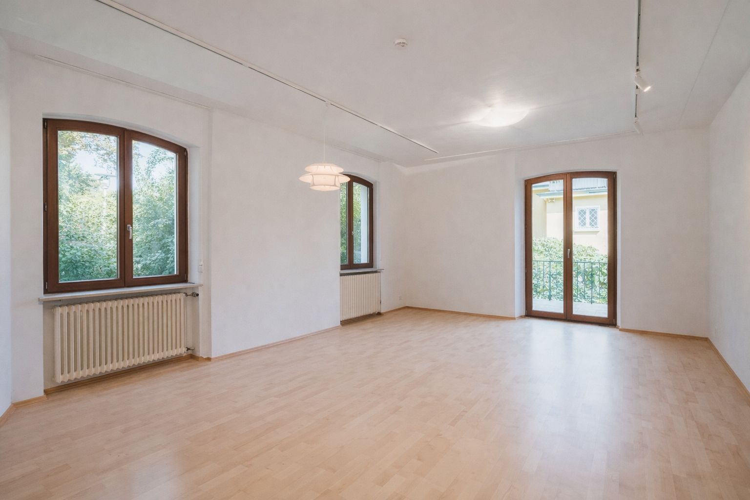 Helles, leeres Zimmer mit Parkettboden, drei Fenstern und einer Glastür zum Balkon.