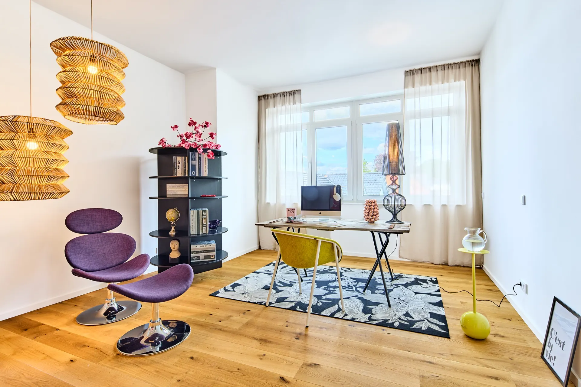 Helles Arbeitszimmer mit Schreibtisch, Stuhl, Regal, lila Sessel und großen Fenstern.