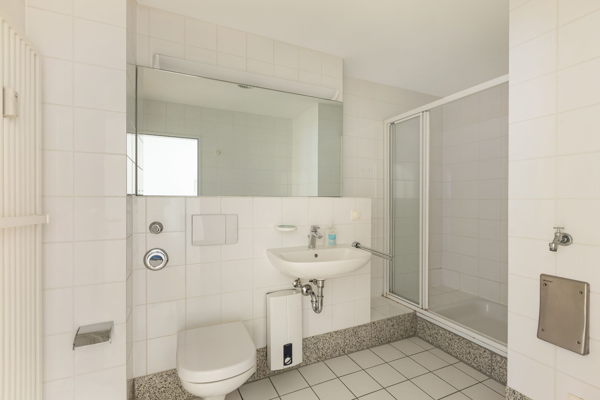 Modernes Badezimmer mit Toilette, Waschbecken, großem Spiegel und Dusche mit Glastür.
