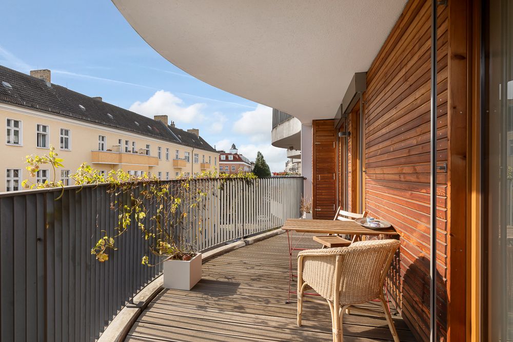 Holzbalkon mit Tisch, Stuhl und Pflanze, Blick auf Wohnhäuser.