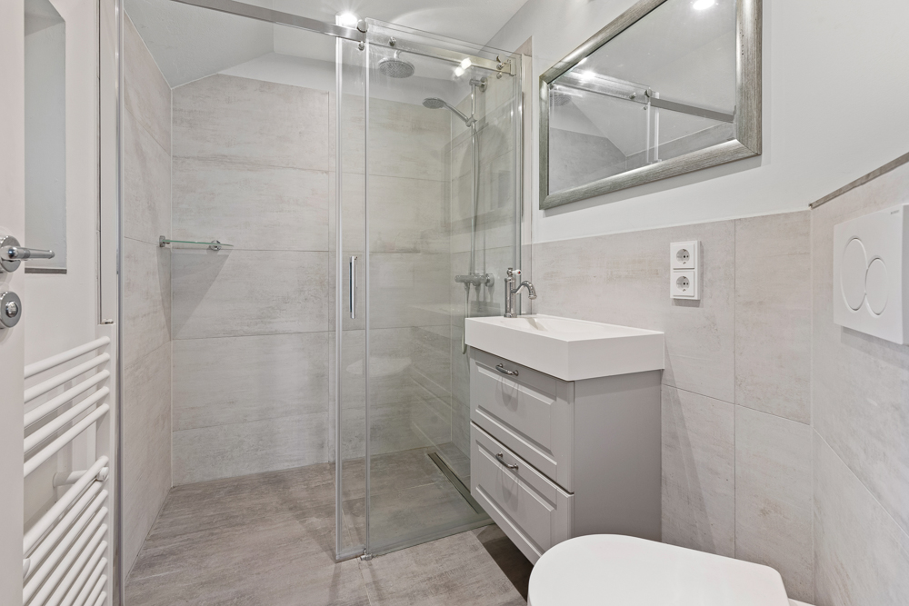 Modernes Badezimmer mit großer Dusche, Waschbecken mit Unterschrank und Spiegel.