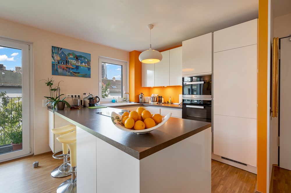Moderne Küche mit weißer Einrichtung, orangener Wand und Schale mit Orangen auf der Arbeitsplatte.