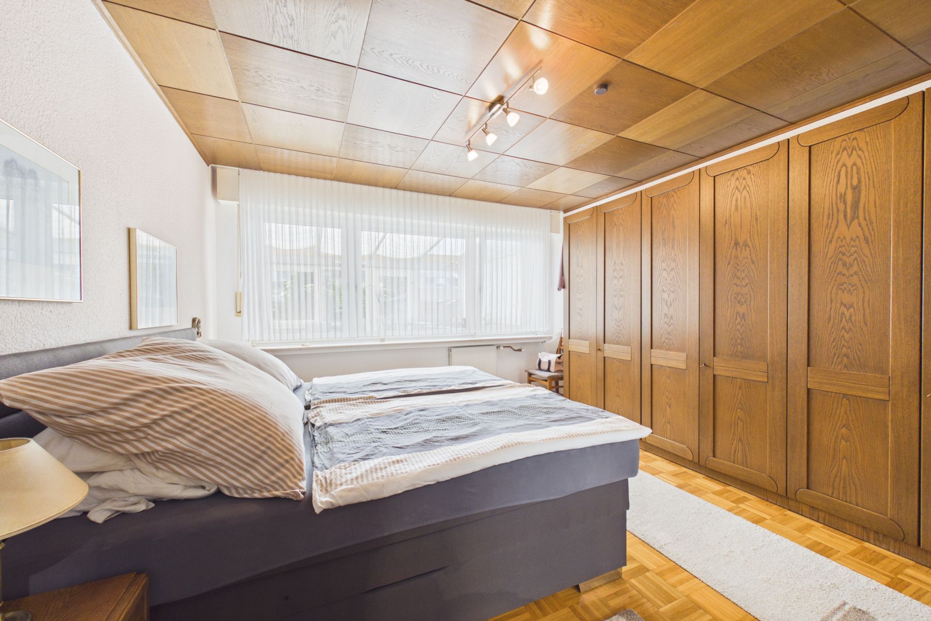 Helles Schlafzimmer mit Doppelbett, großem Fenster und mehreren Holzschränken.