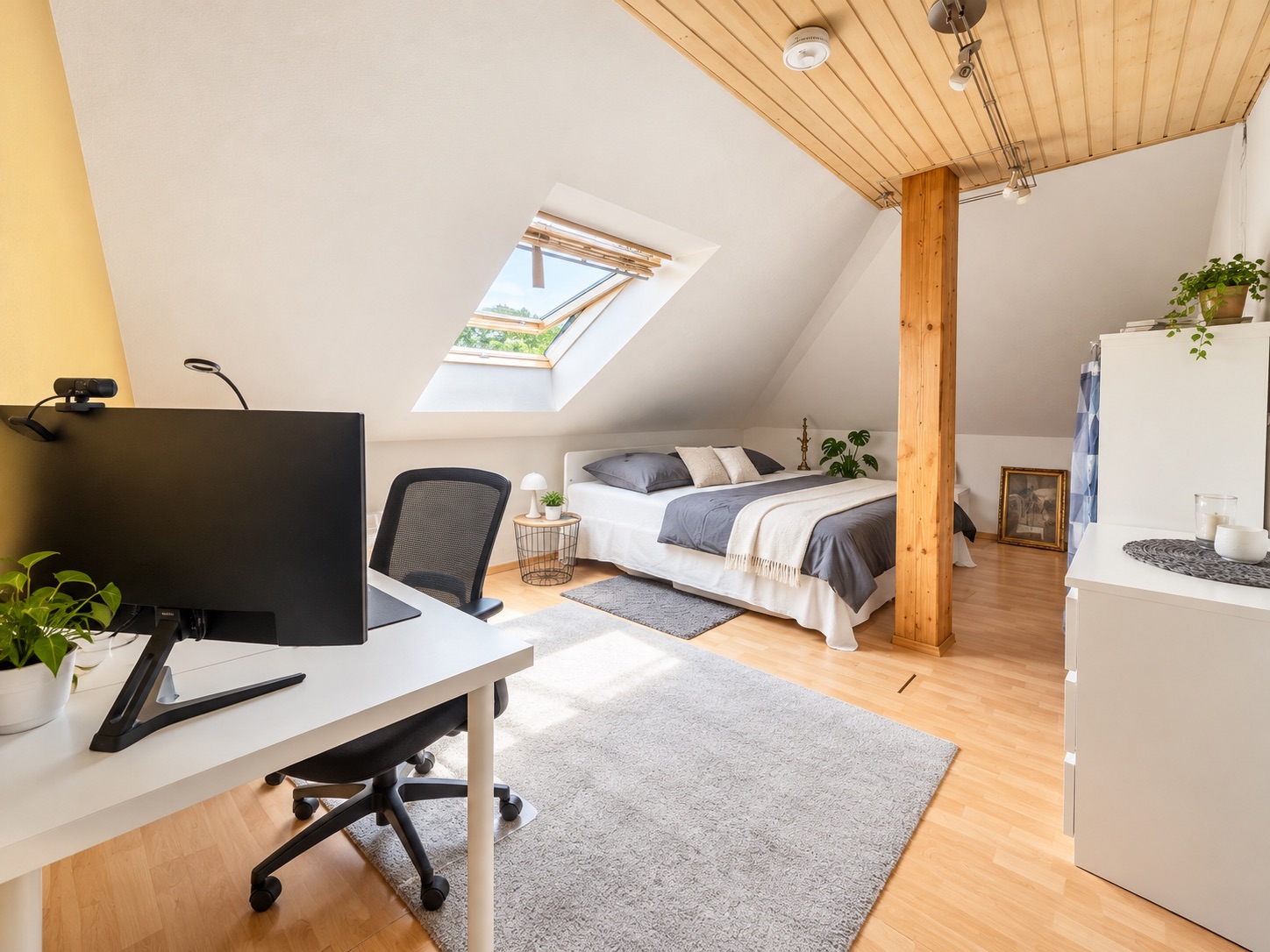 Helles Schlafzimmer im Dachgeschoss mit Bett, Schreibtisch und schrägem Fenster.