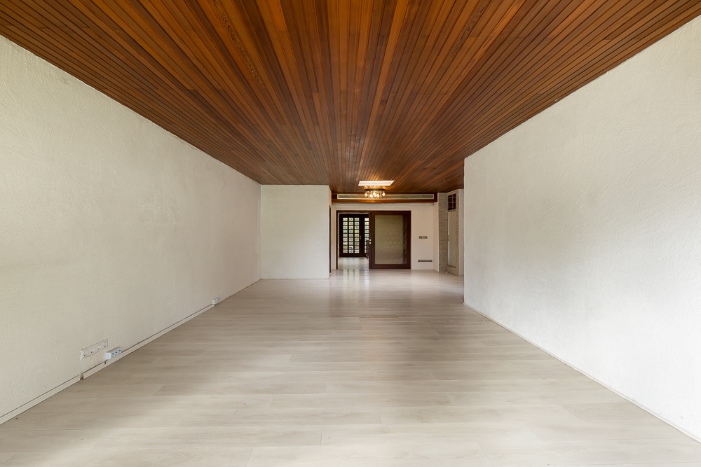Großer, leerer Raum mit heller Holzboden und Holzdecke, weiße Wände, Tür im Hintergrund.