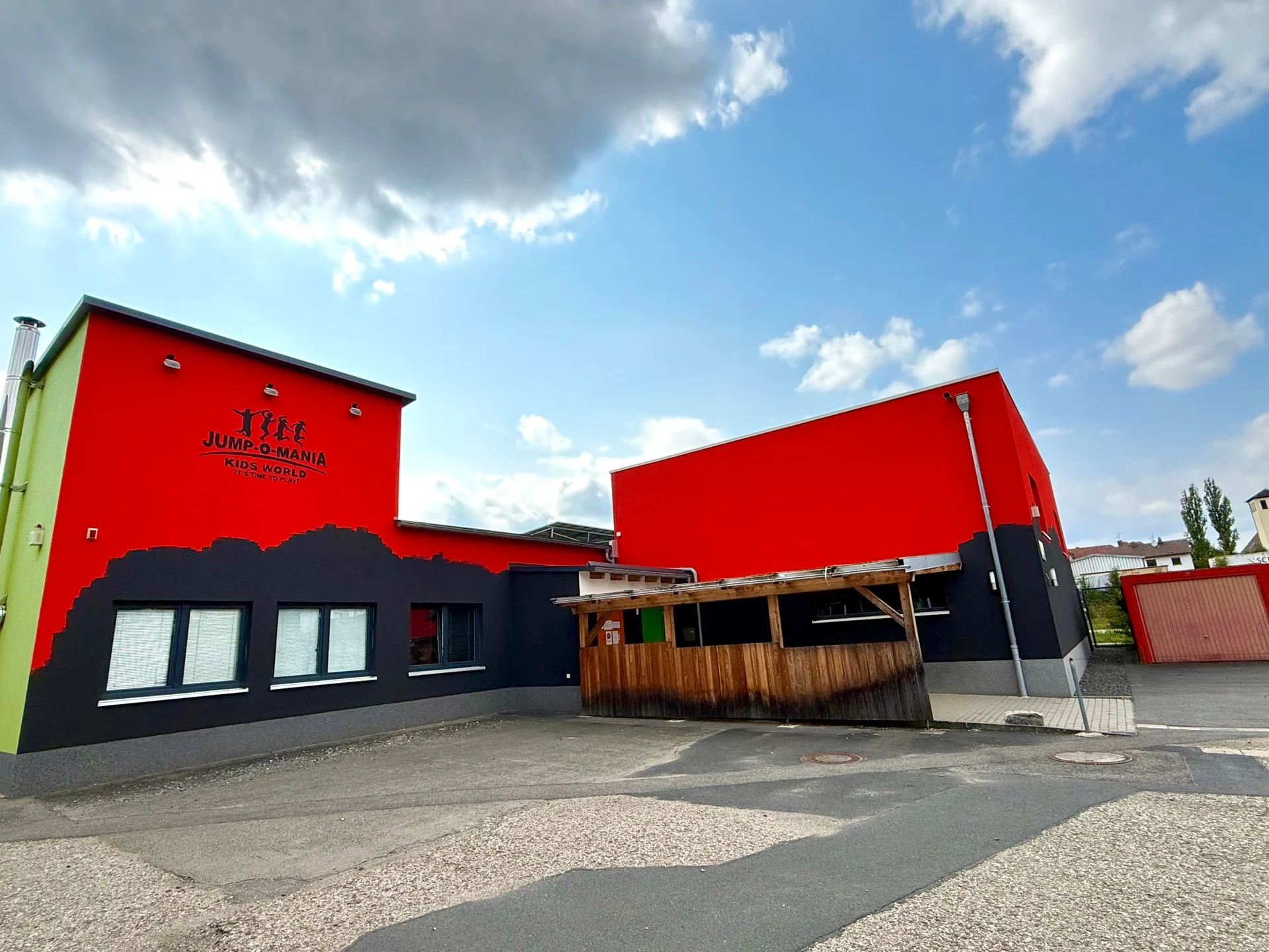 Zweistöckiges Gebäude mit roter und schwarzer Fassade, davor ein hölzerner Unterstand auf dem Hof.