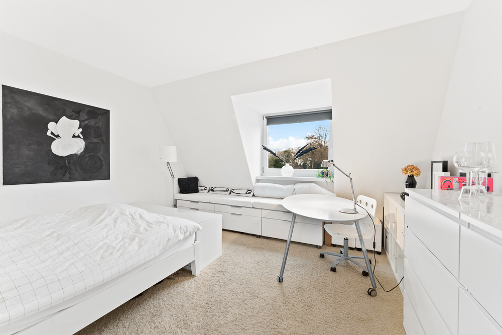 Helles Schlafzimmer mit Bett, Schreibtisch, Kommode und Fenster mit Ausblick.