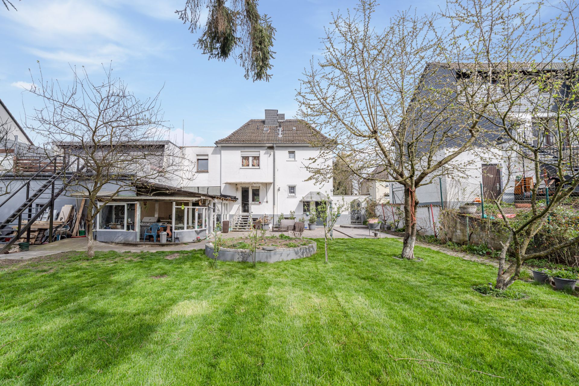 Großer Garten mit Rasenfläche, Bäumen und Blick auf ein weißes Wohnhaus mit Terrasse.