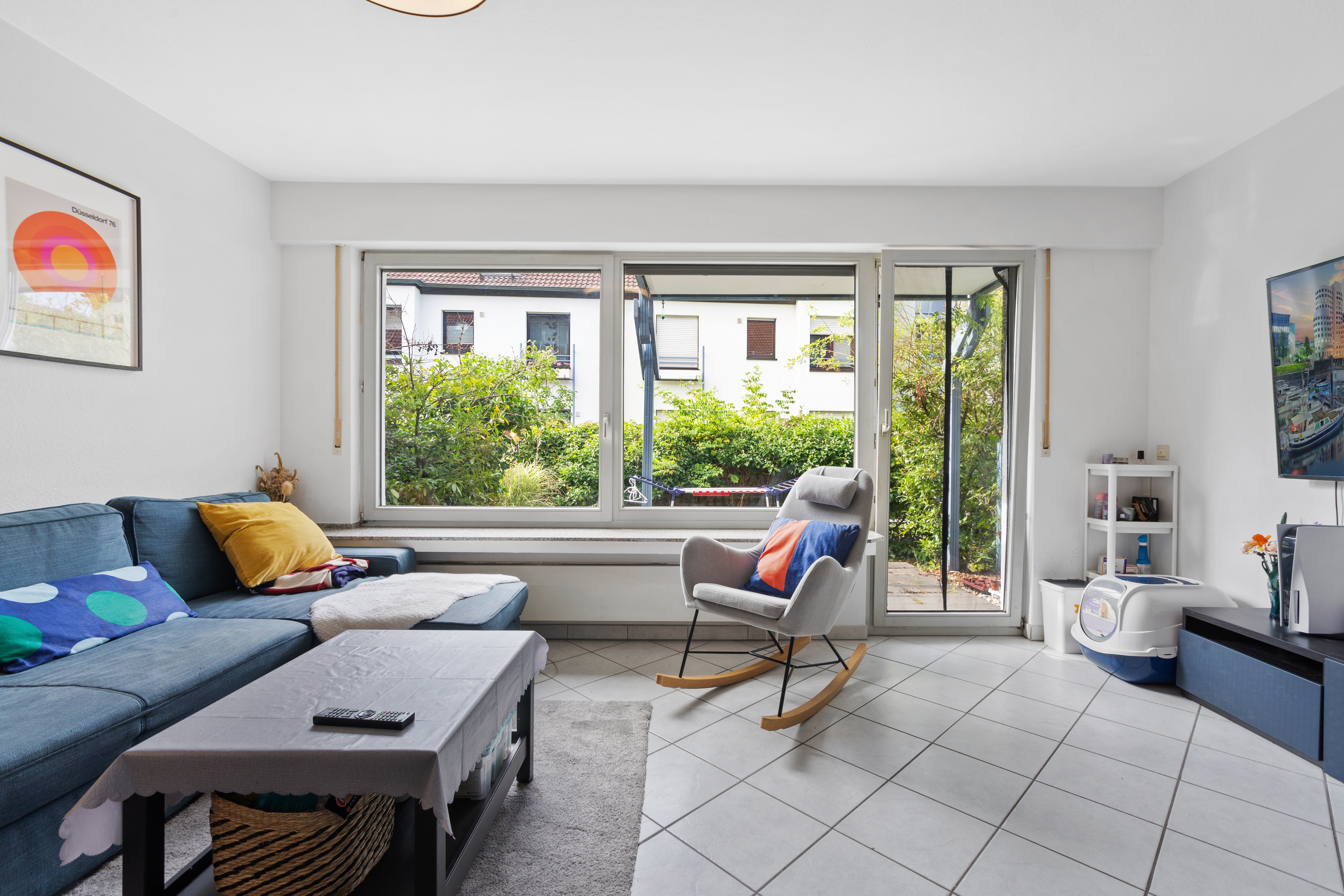 Helles Wohnzimmer mit blauem Sofa, Schaukelstuhl und großem Fenster zum Garten.