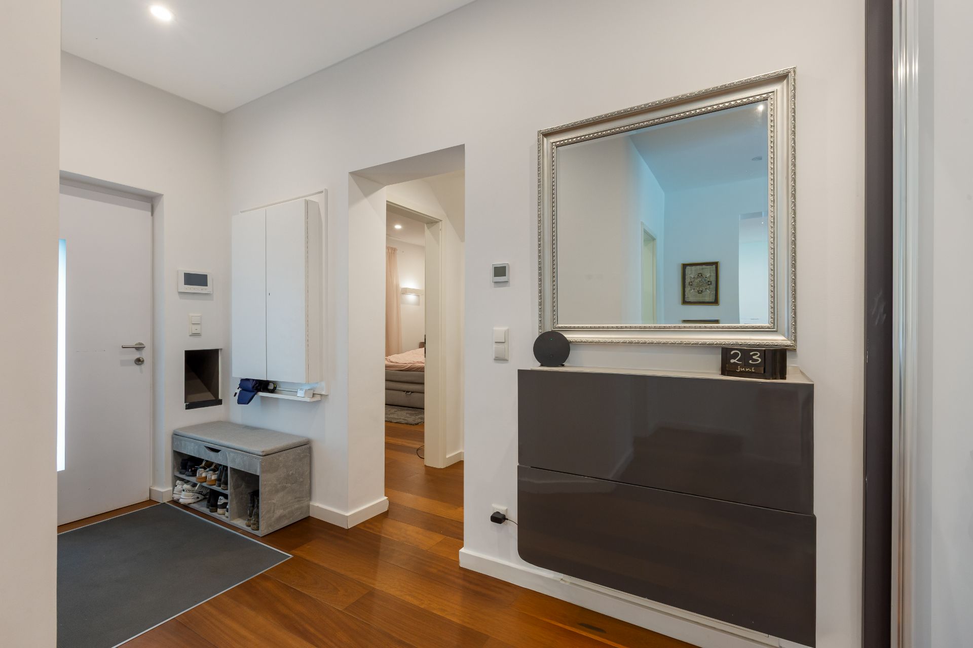 Moderner Flur mit Spiegel, Wandregal, Schrank und Holzboden.
