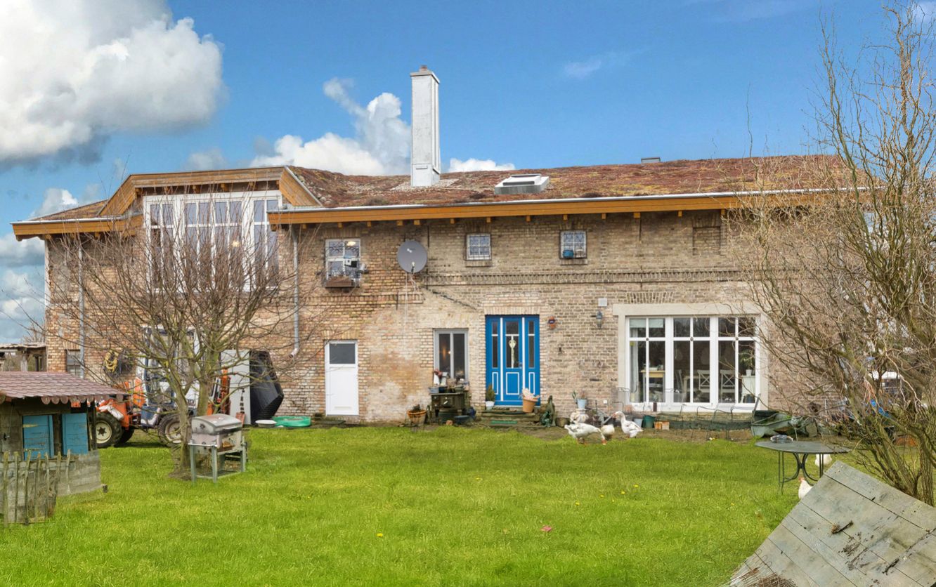 Backsteinwohnhaus mit blauem Eingang, großem Garten und Hühnern im Vordergrund.