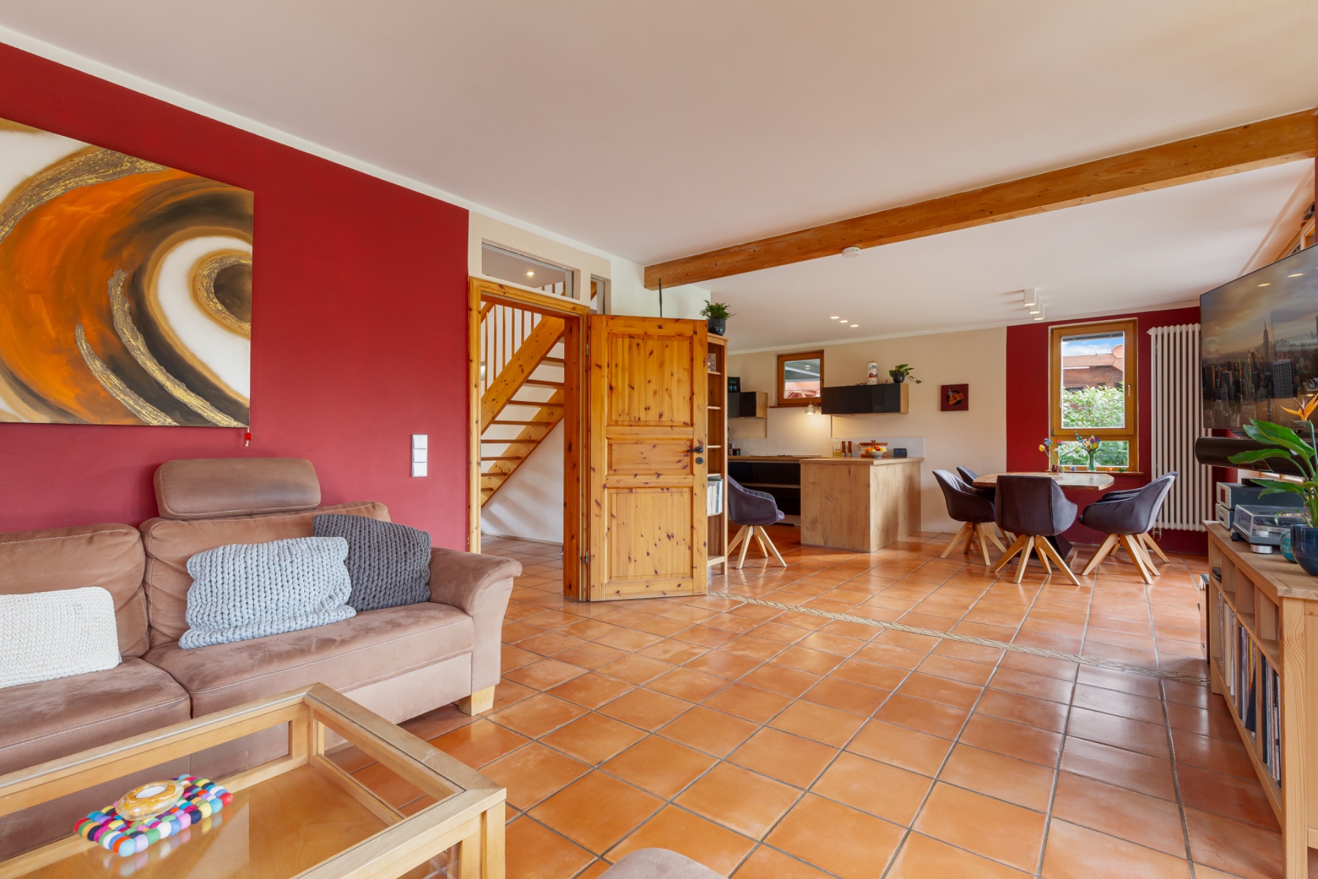 Helles Wohnzimmer mit braunem Sofa, Esstisch, offener Küche und Holztreppe.