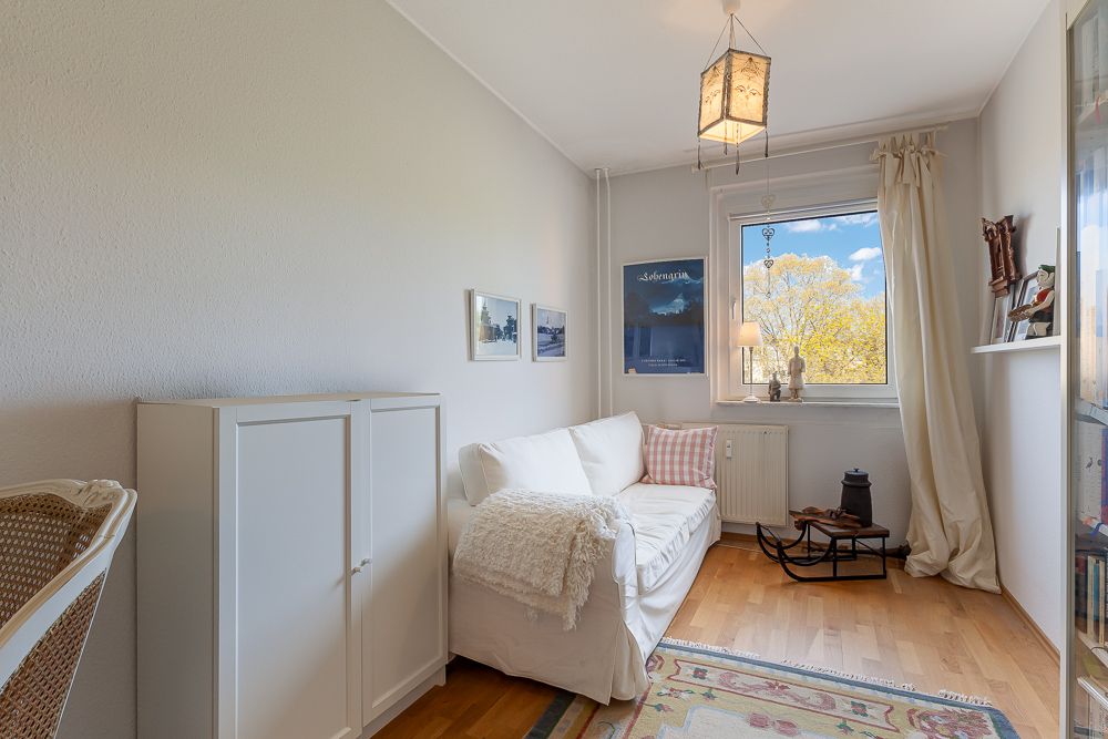 Kleines Wohnzimmer mit weißem Sofa, Teppich, Fenster und Wandbildern.
