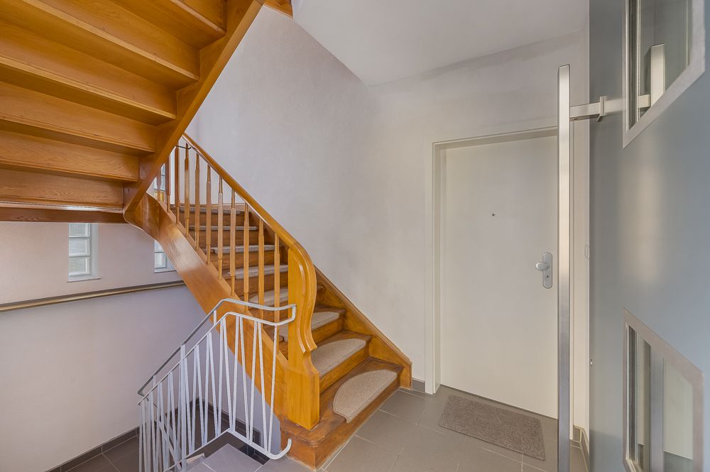Eingangsbereich mit Holztreppe, weißer Tür, Fliesenboden und Geländer.