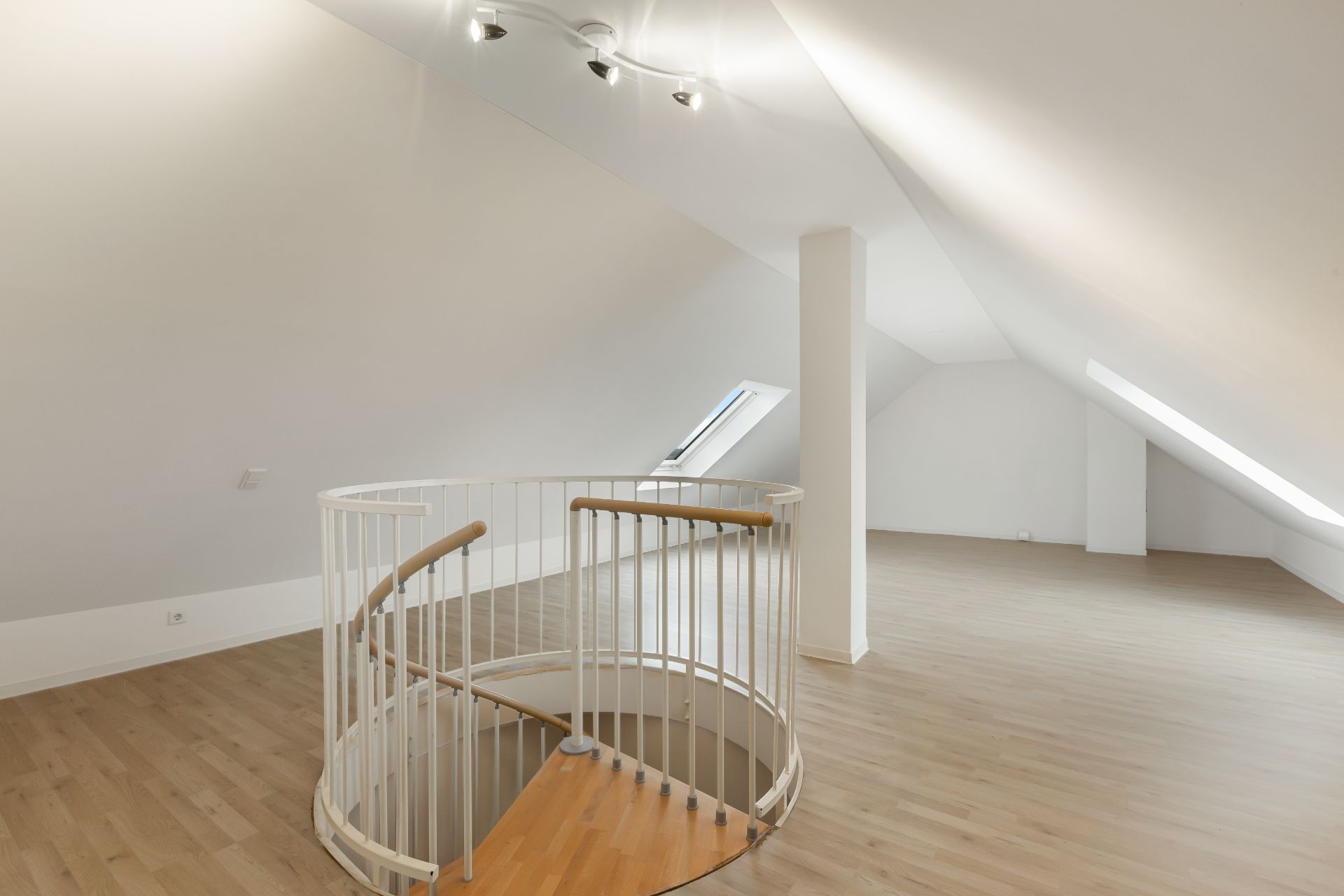 Helles Dachgeschosszimmer mit Holzfußboden und runder Treppe in der Mitte.