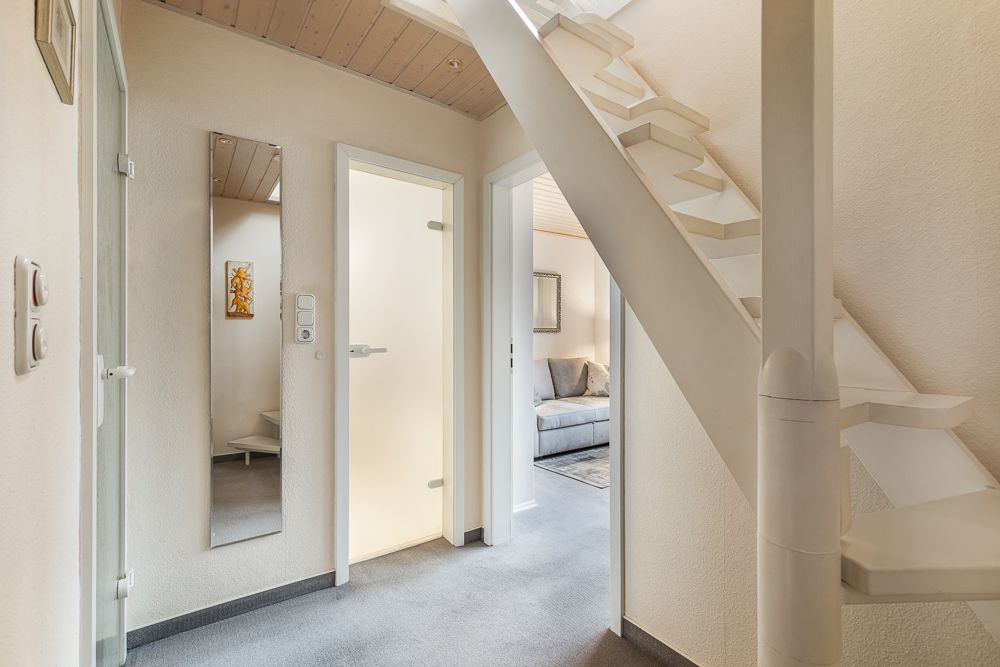 Heller Flur mit Spiegel, weißen Türen und einer weißen Treppe nach oben.