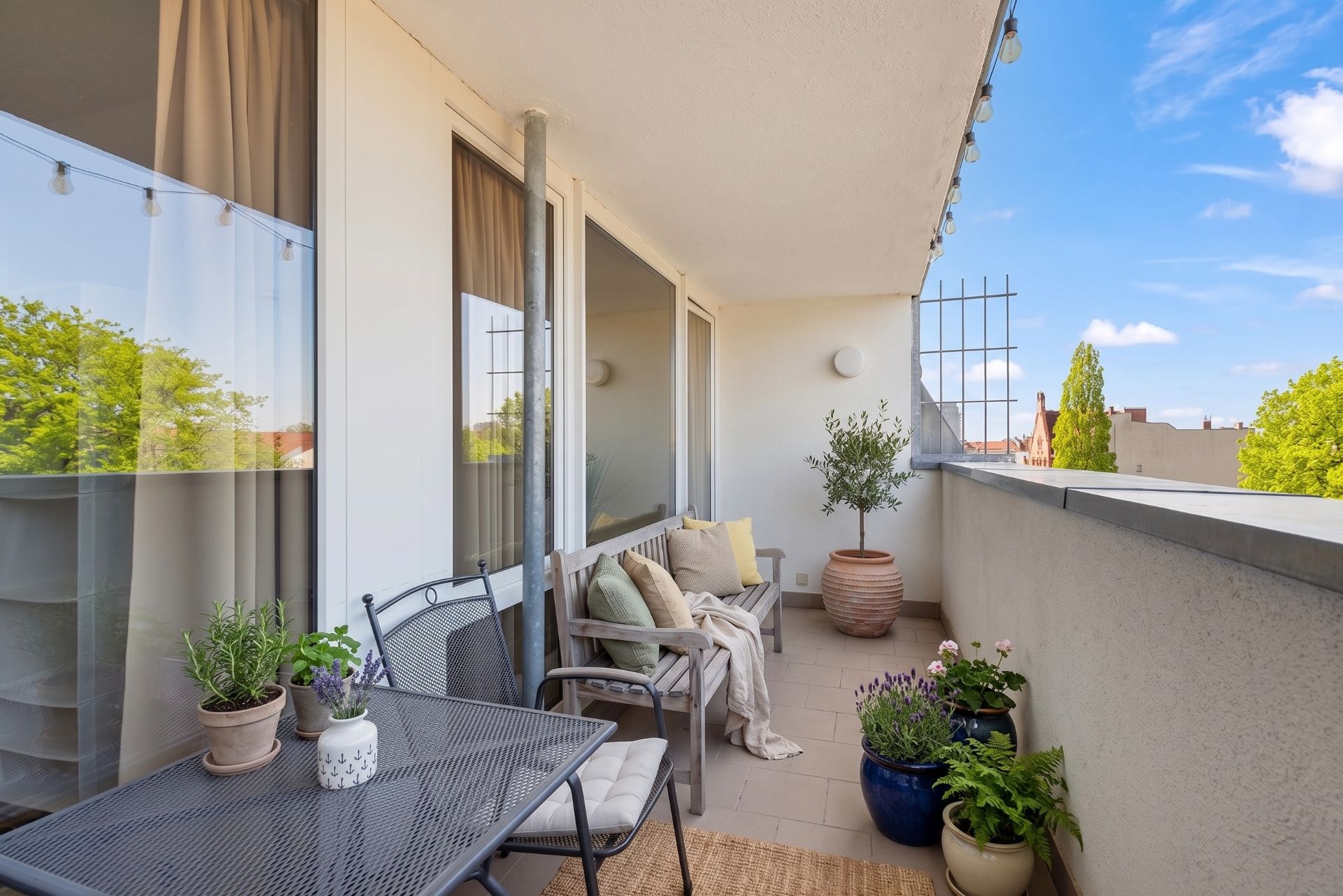 Heller Balkon mit Sitzgelegenheiten, Tisch, Pflanzen und Ausblick auf Bäume.