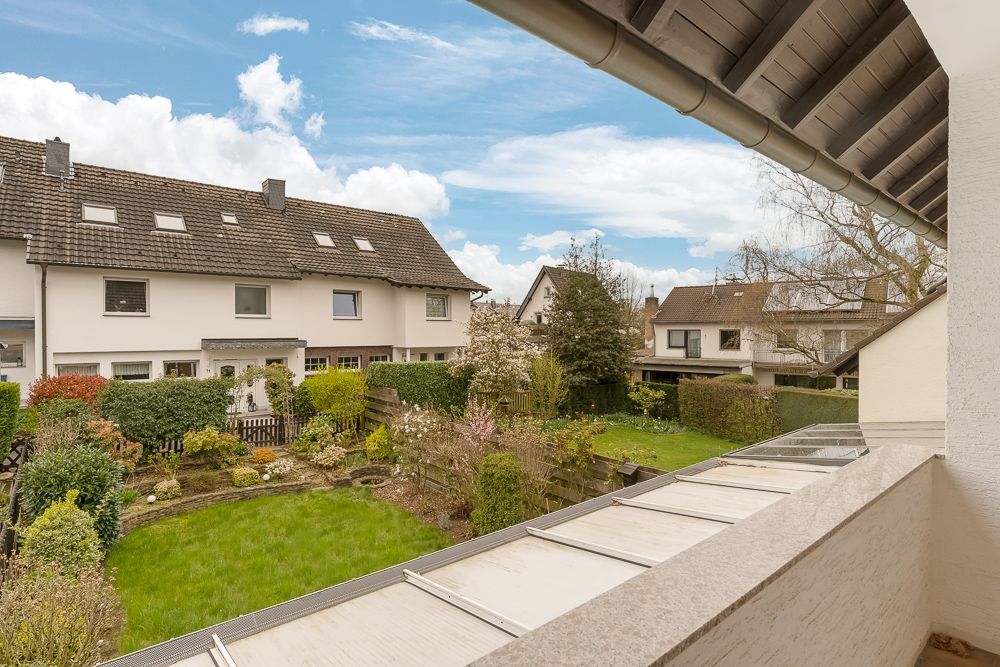 Blick von einem Balkon auf einen Garten mit Rasen, Büschen und Nachbarhäusern.