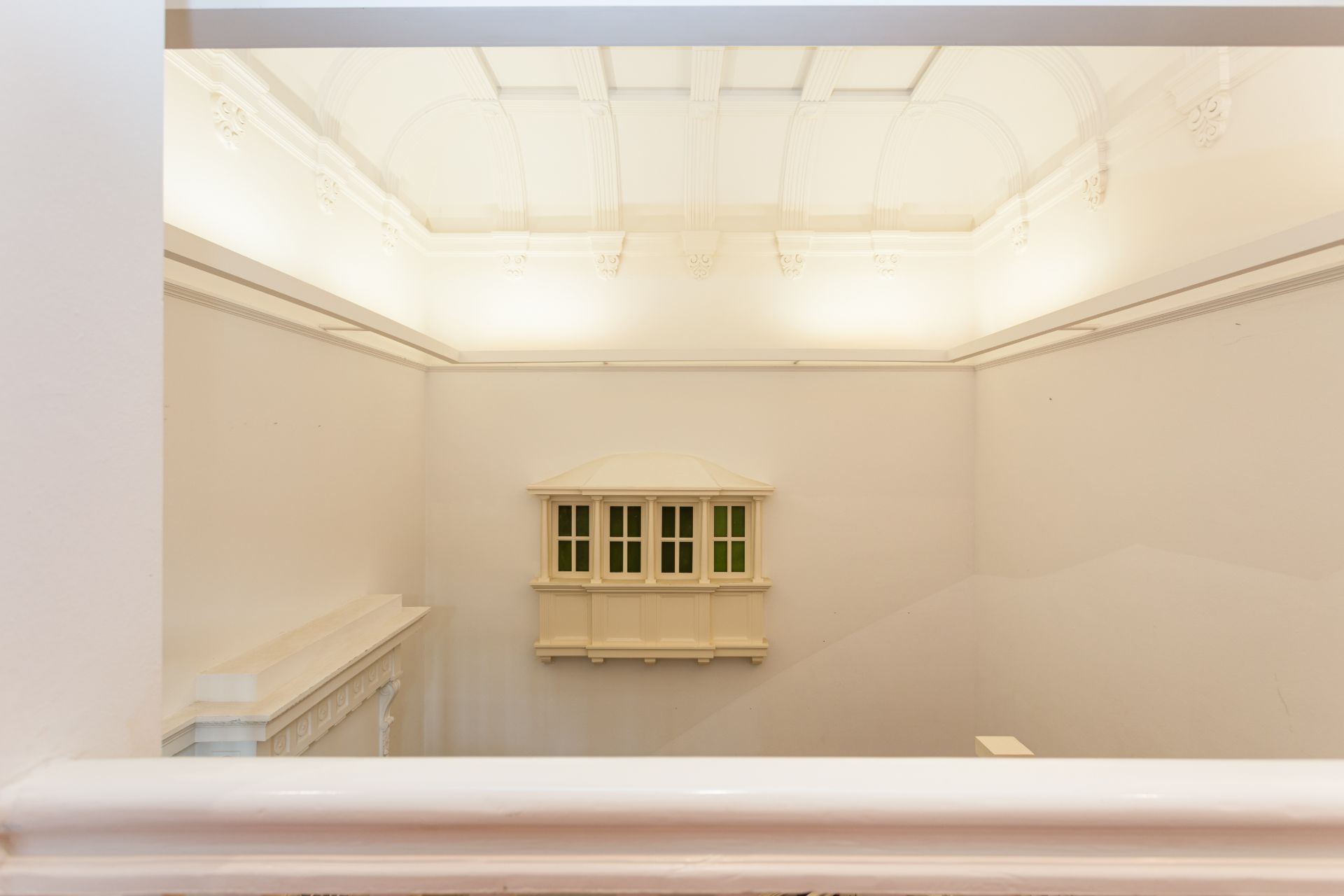 Heller Innenraum mit hohen Wänden und kleinem Fenster mit grünen Scheiben in der Mitte.