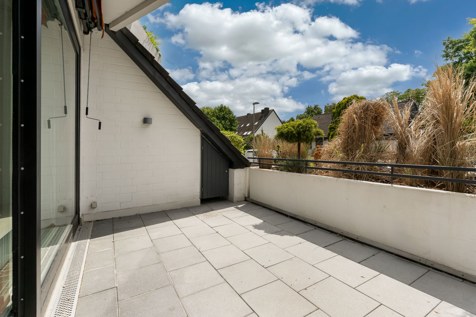 Große Terrasse mit Fliesenboden, weißer Wand und Blick auf Nachbargärten.