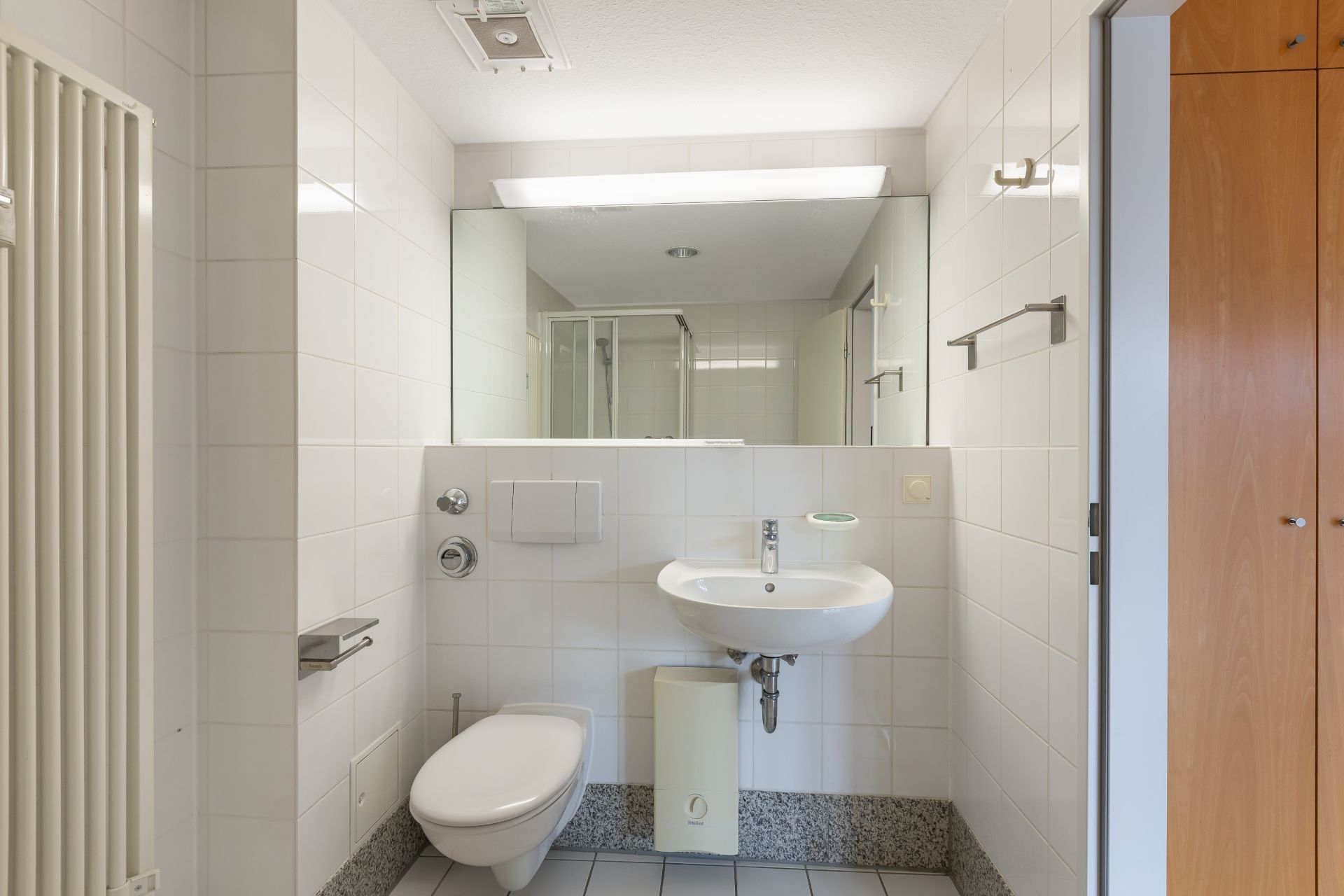 Helles Badezimmer mit WC, Waschbecken, großem Spiegel und Handtuchheizkörper.